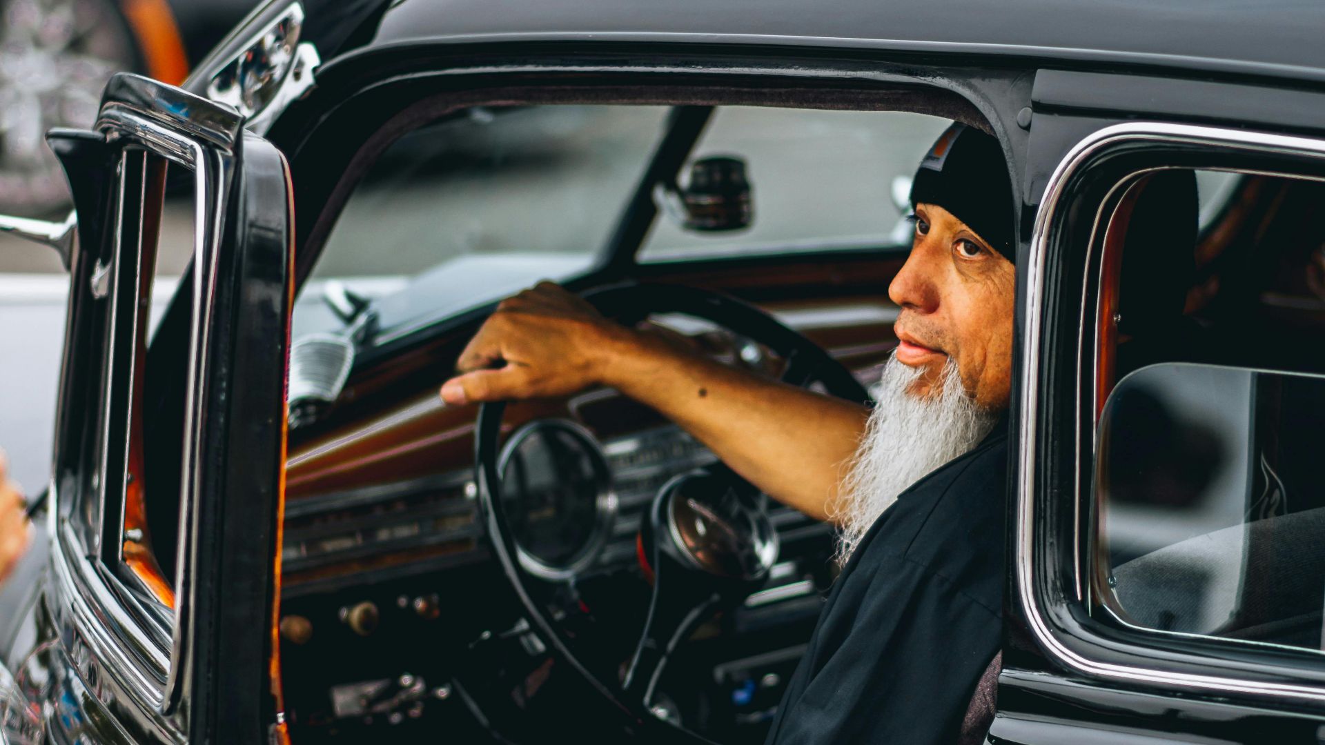 Bearded man behind the wheel of a vintage car at a Los Angeles car show, showcasing automobile culture.