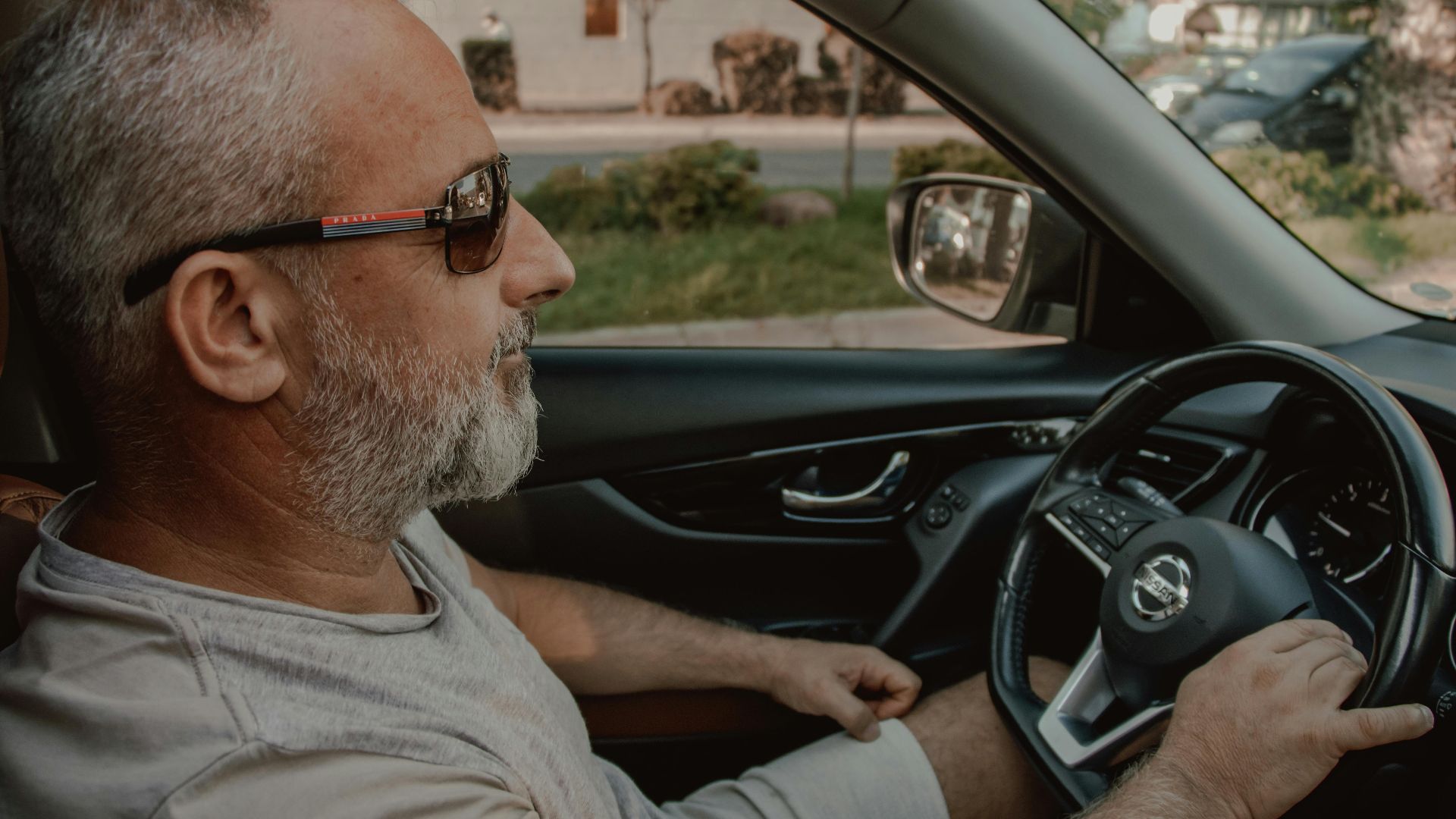 Middle-aged man driving a car wearing sunglasses, providing a relaxed and confident vibe.