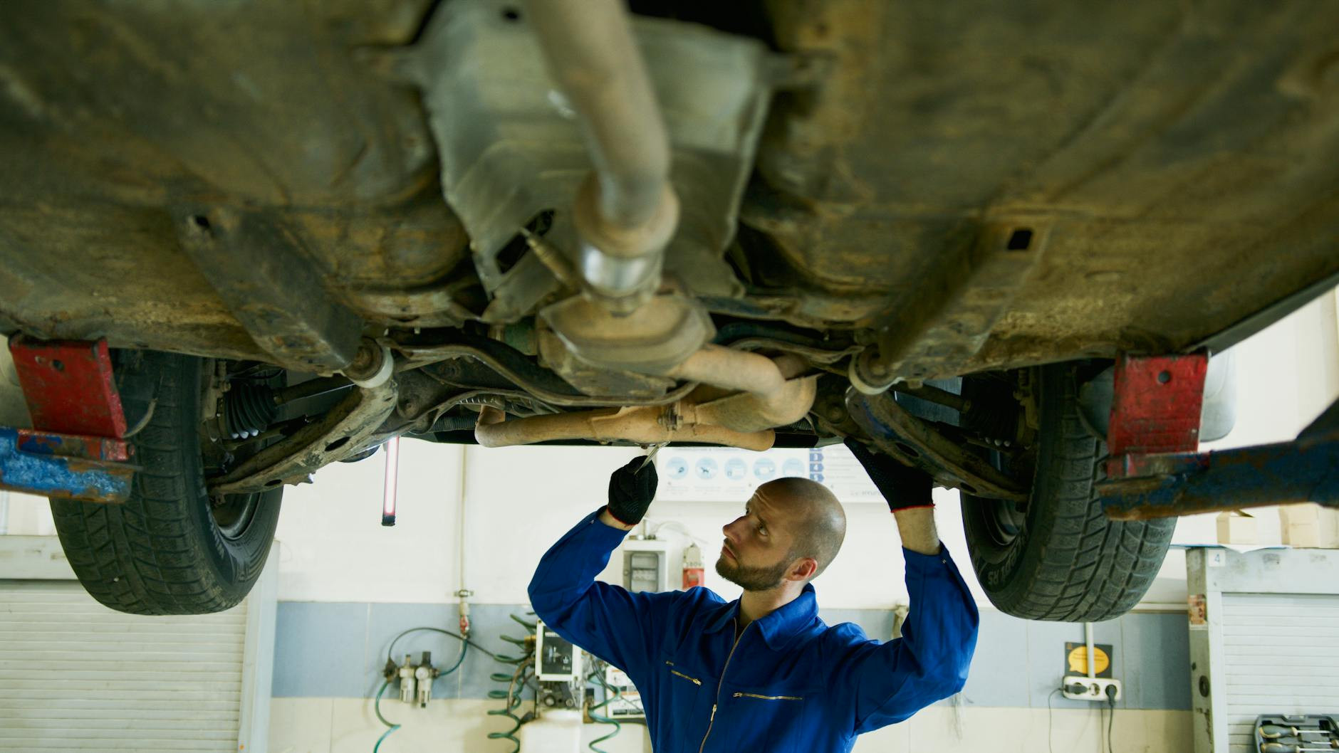 Mechanic examining the underside of a car in an auto repair shop for maintenance.