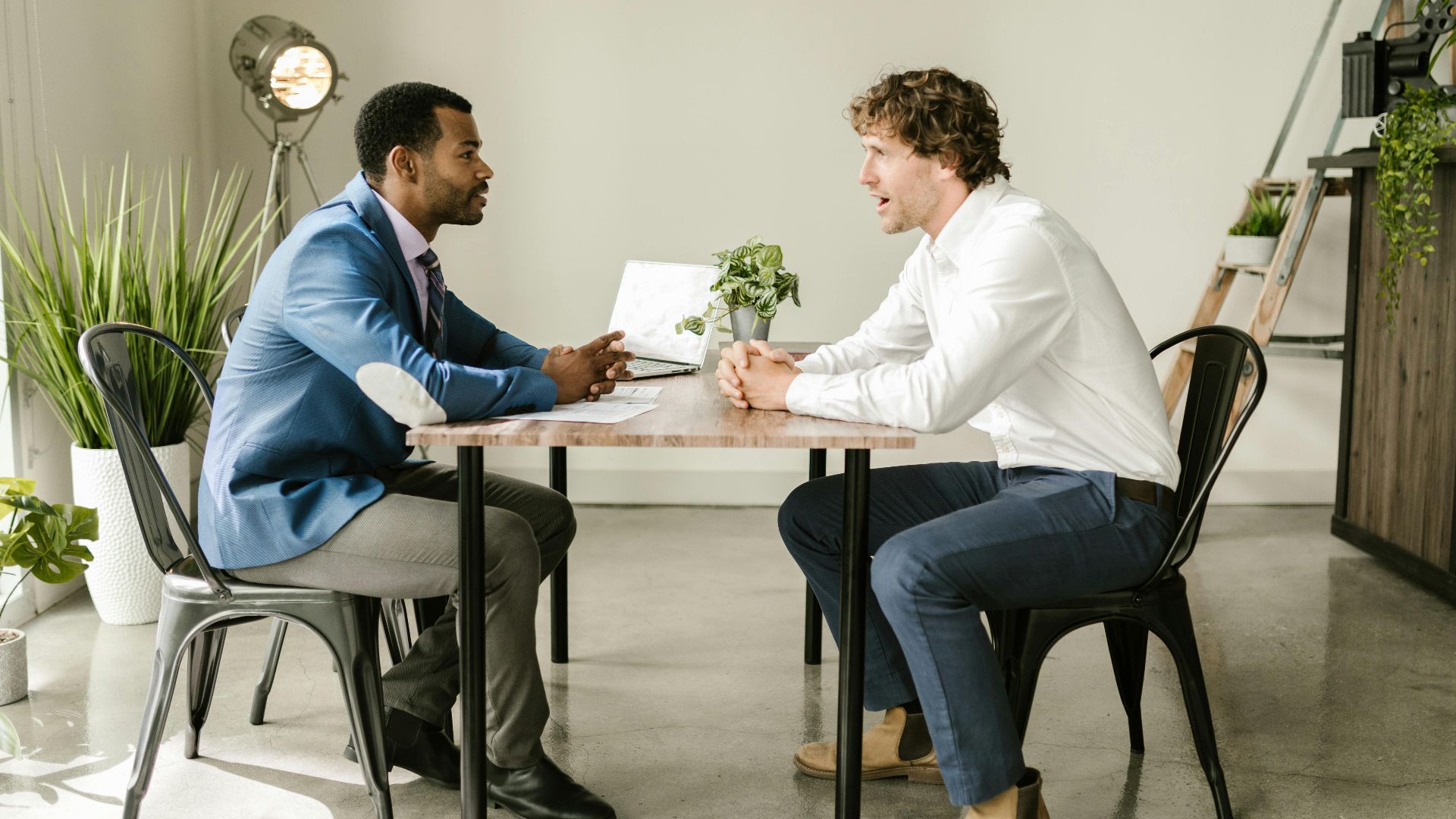 Two businessmen engaged in a professional discussion at an indoor office setting with greenery and modern decor.