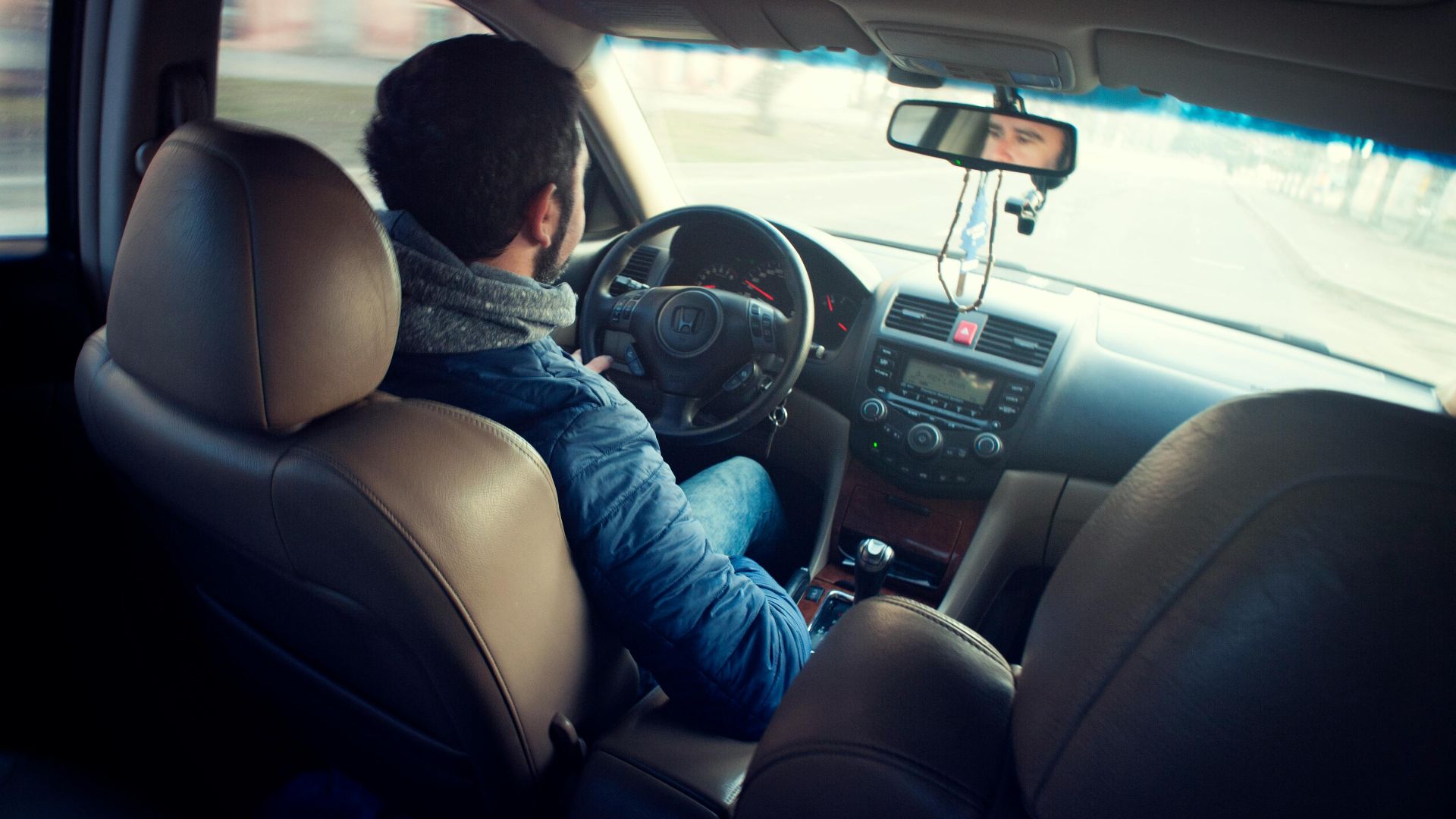 A man driving a car with focus on interior, dashboard, and steering wheel, captured from the backseat.