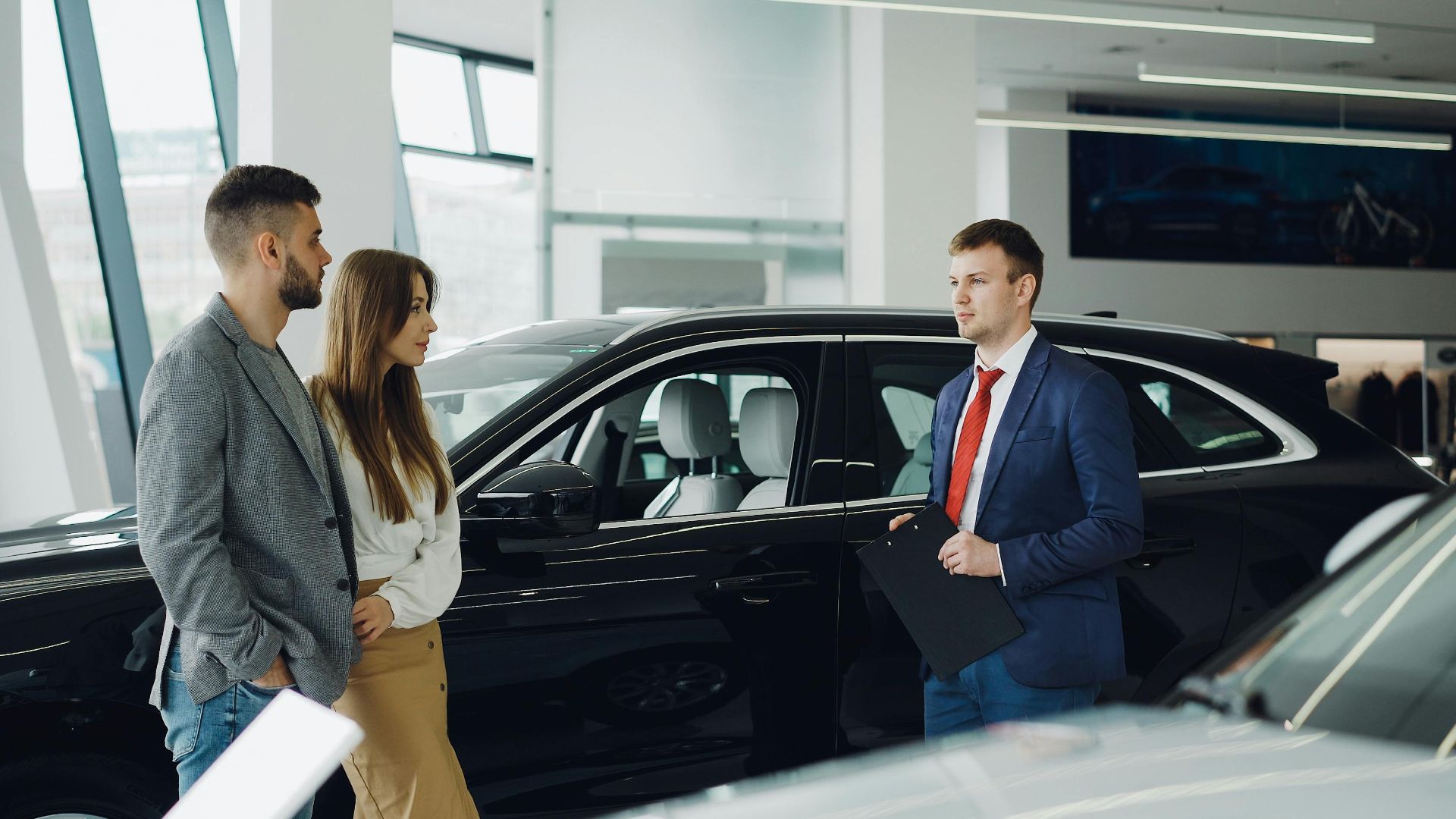 Salesperson assisting couple in modern car showroom.