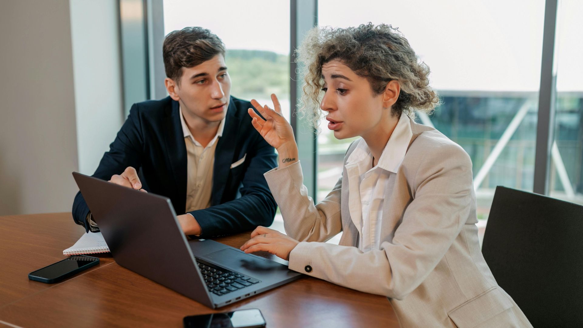 Two business professionals discussing ideas at a wooden table inside a modern office environment.