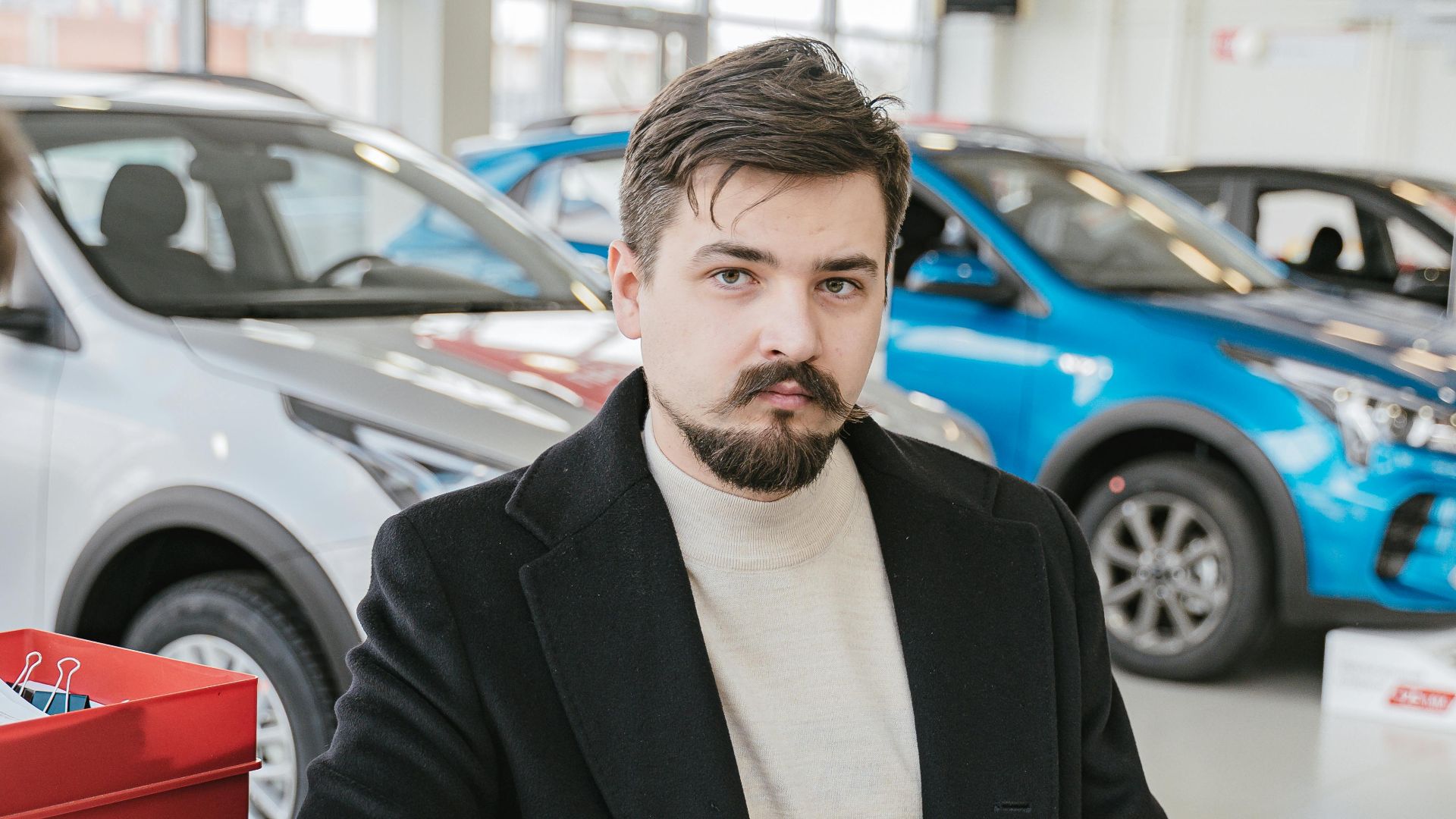 A man in a coat discusses with a sales representative in a bright, modern car showroom.