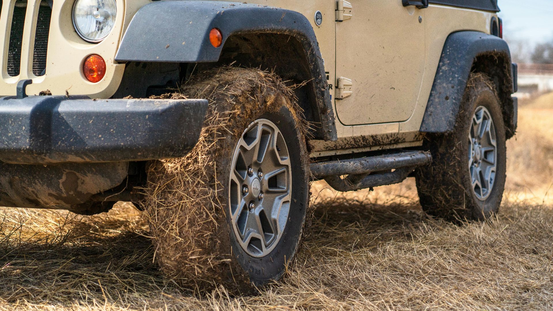 Close-up of an off-road vehicle parked in a dry grass field with muddy tires.
