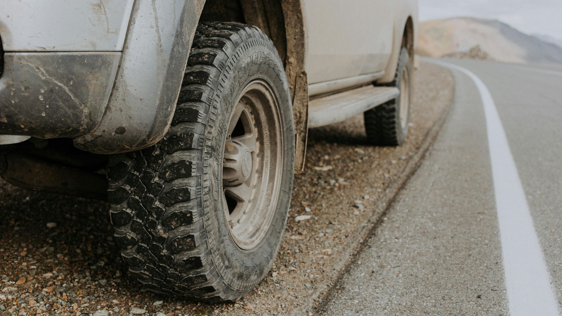 A rugged off-road vehicle's dirty tire on a gravel roadside in Altai Republic, Russia.