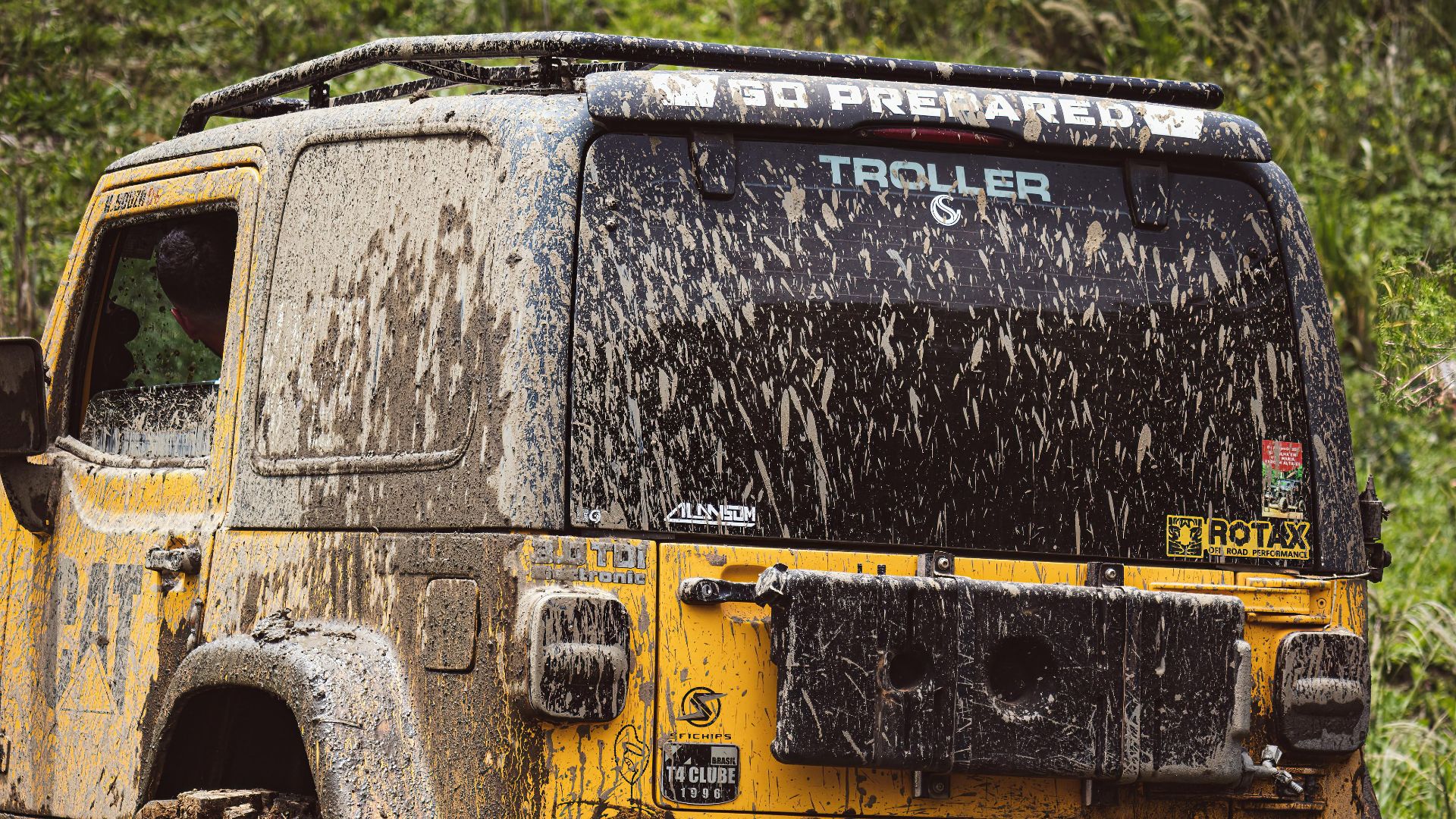 Yellow Troller Jeep covered in mud on a rugged trail, showcasing offroad adventure.