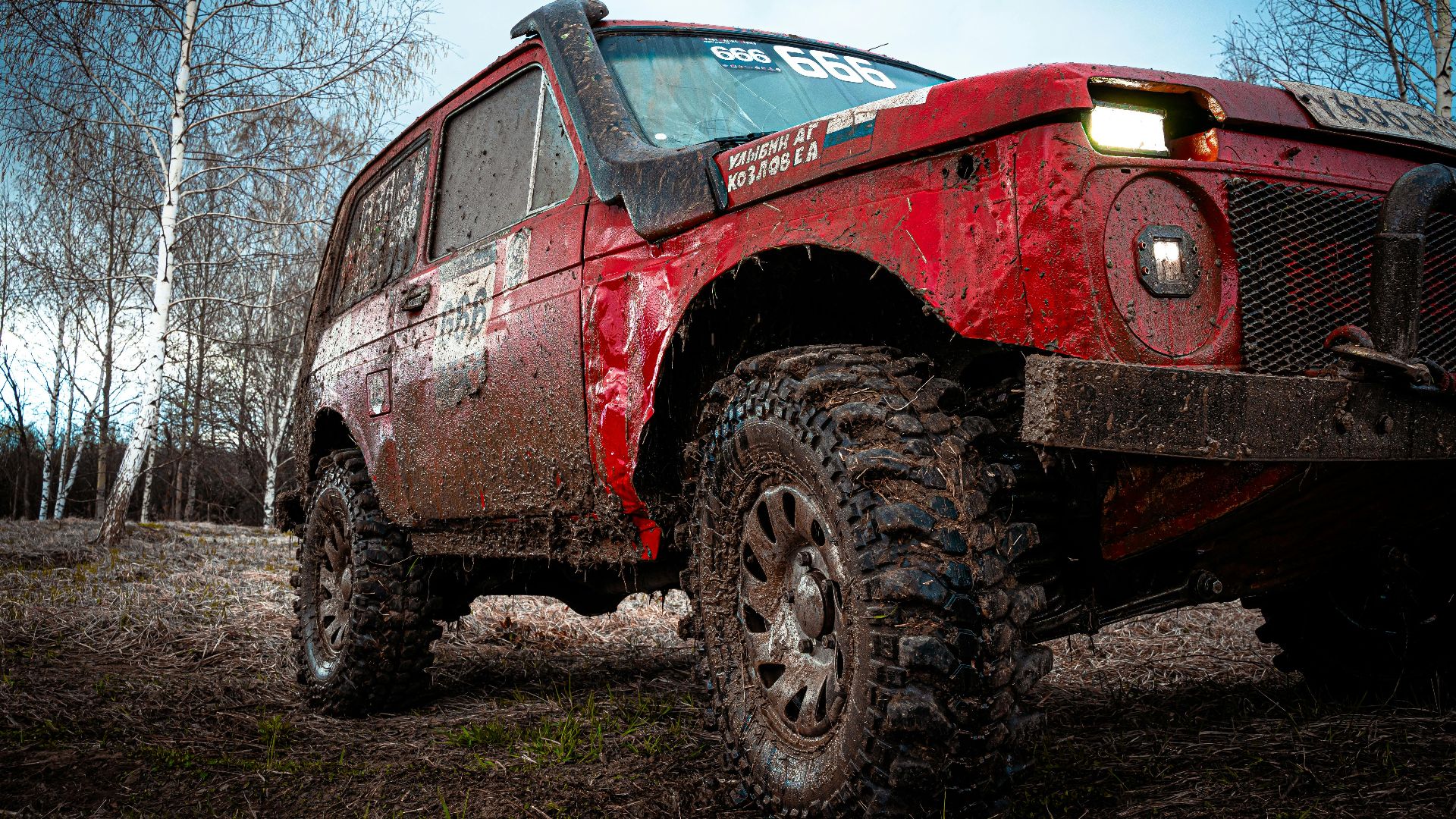 A red 4x4 vehicle navigates a muddy and rural off-road path, showcasing adventure and ruggedness.