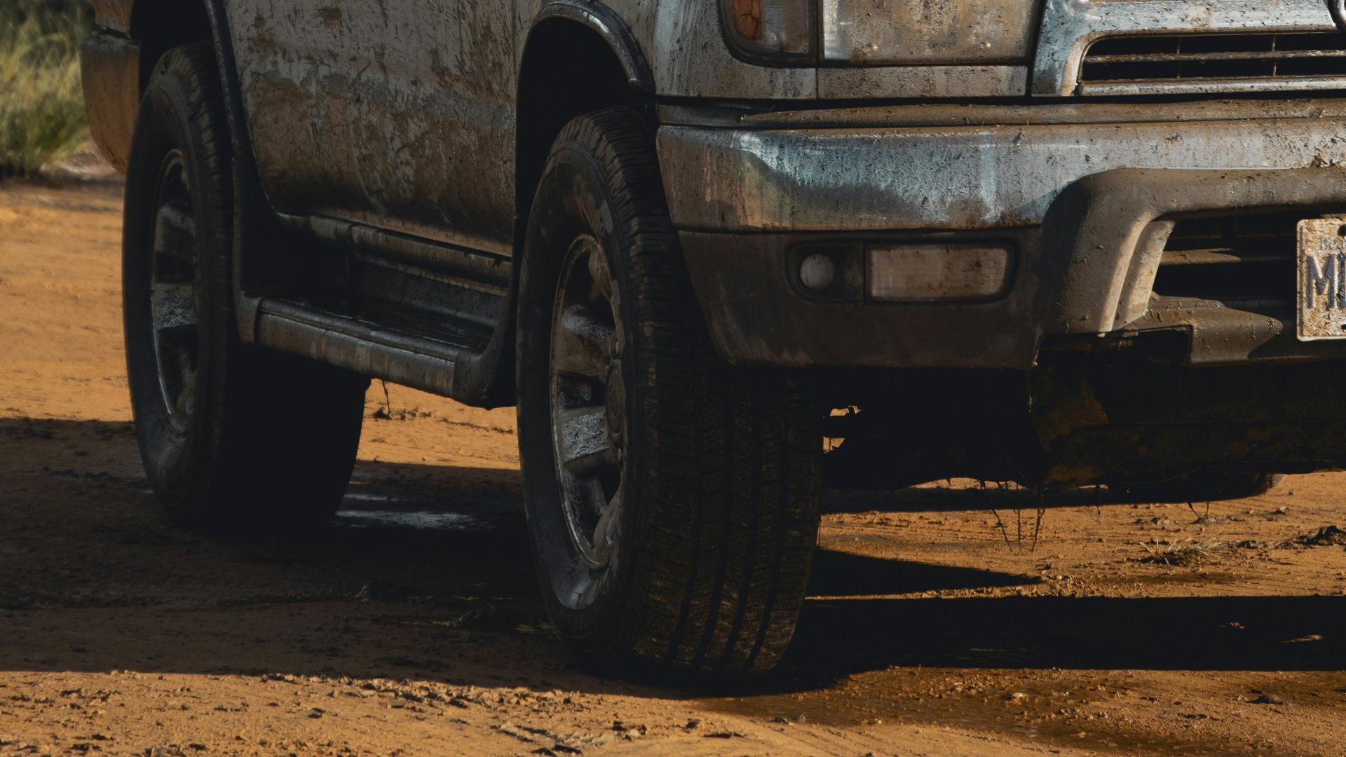 A rugged SUV covered in mud parked on a dirt road surrounded by dense forest.