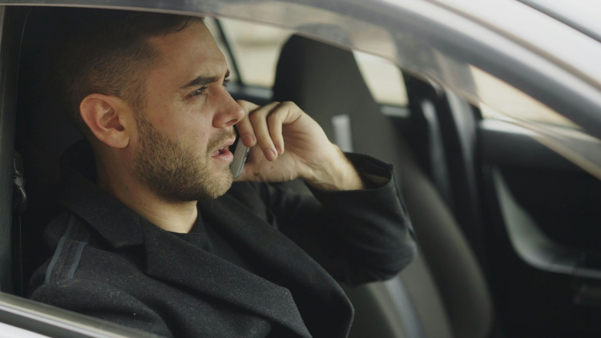 Man in car talking on smartphone, appearing thoughtful.