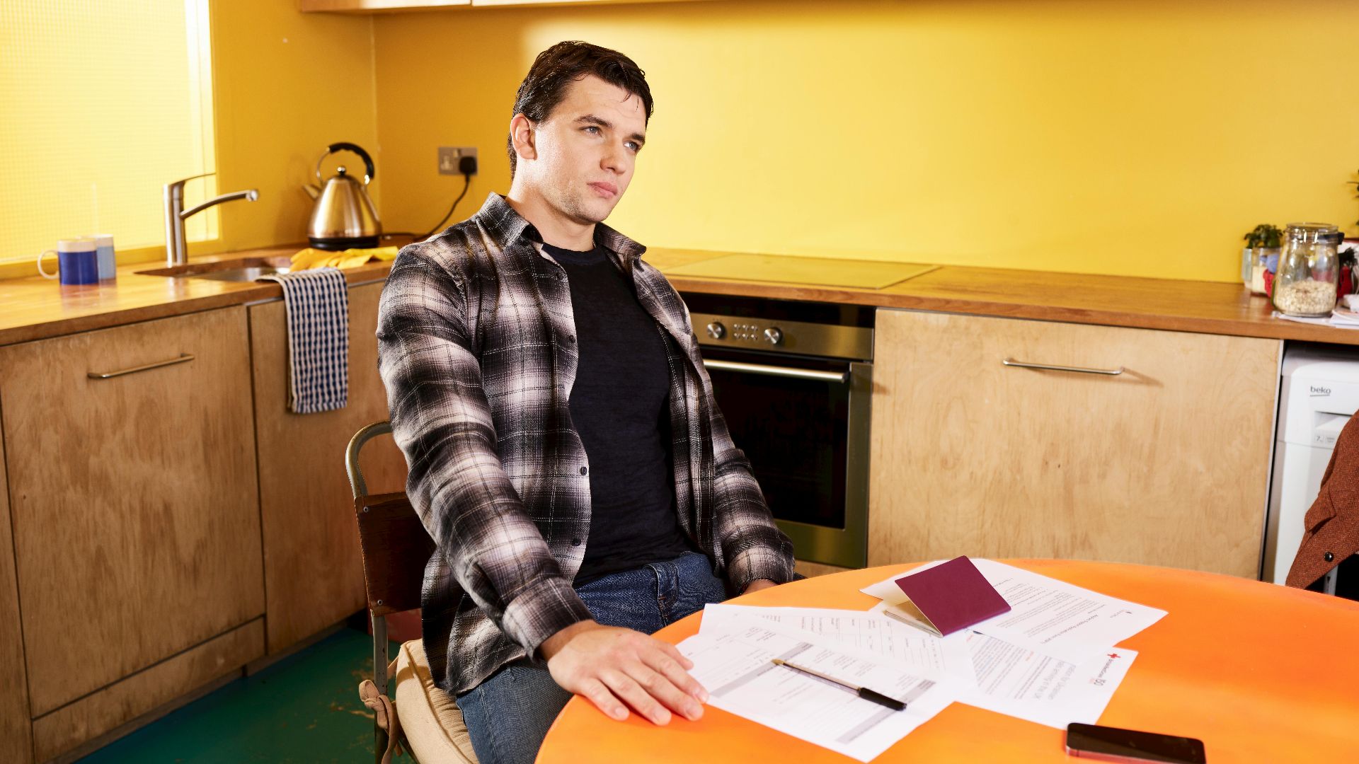 Man sitting at a kitchen table with documents and a passport, contemplating.