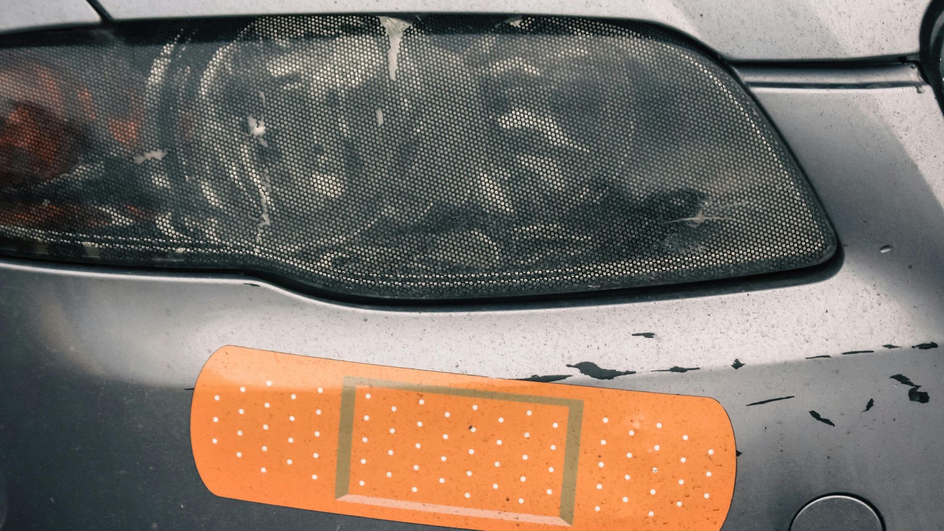 Close-up of a car's headlight with a humorous bandage sticker, suggesting repair.