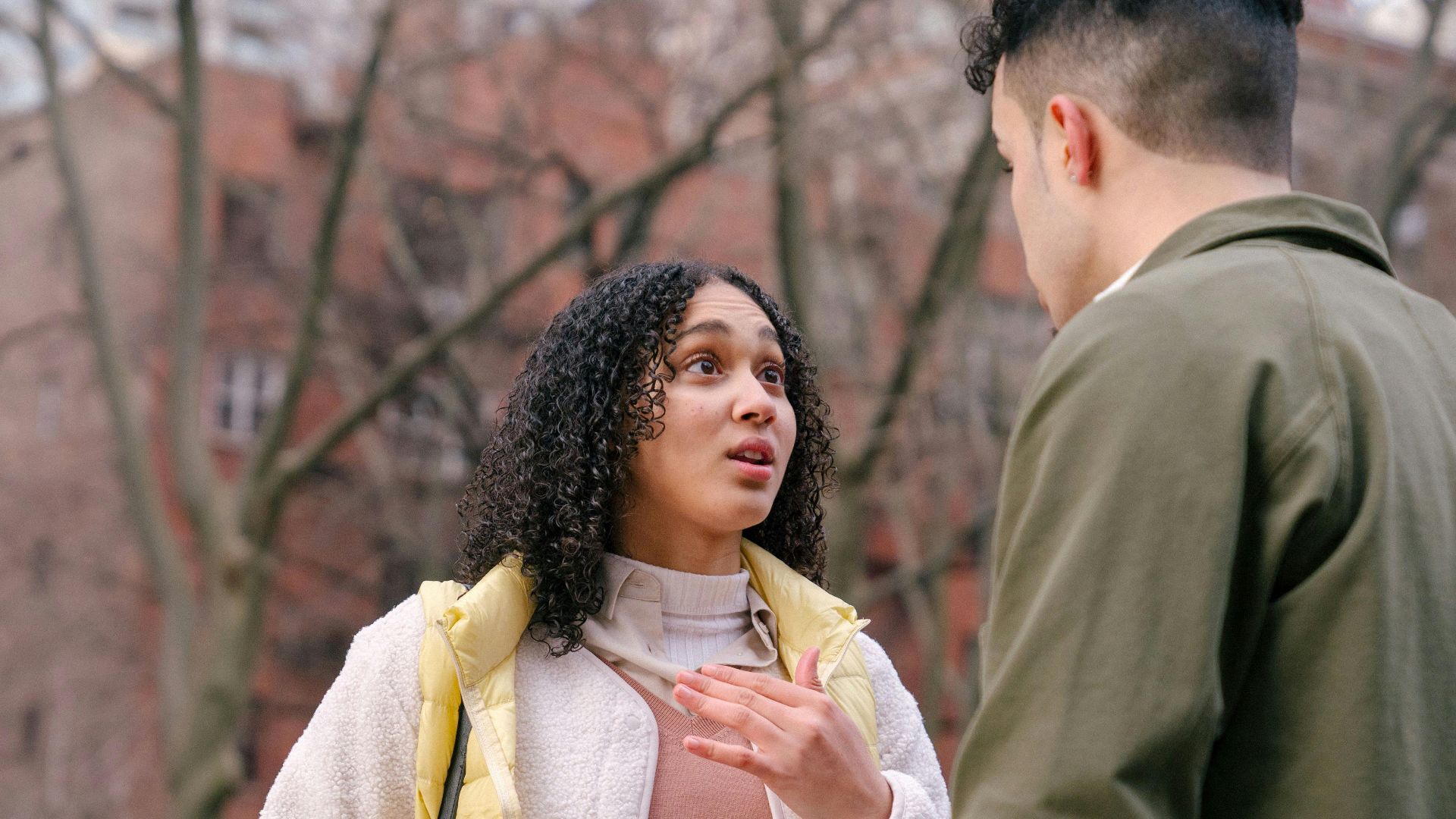 From below of ethnic female with short curly hair standing and arguing with boyfriend on street in daylight