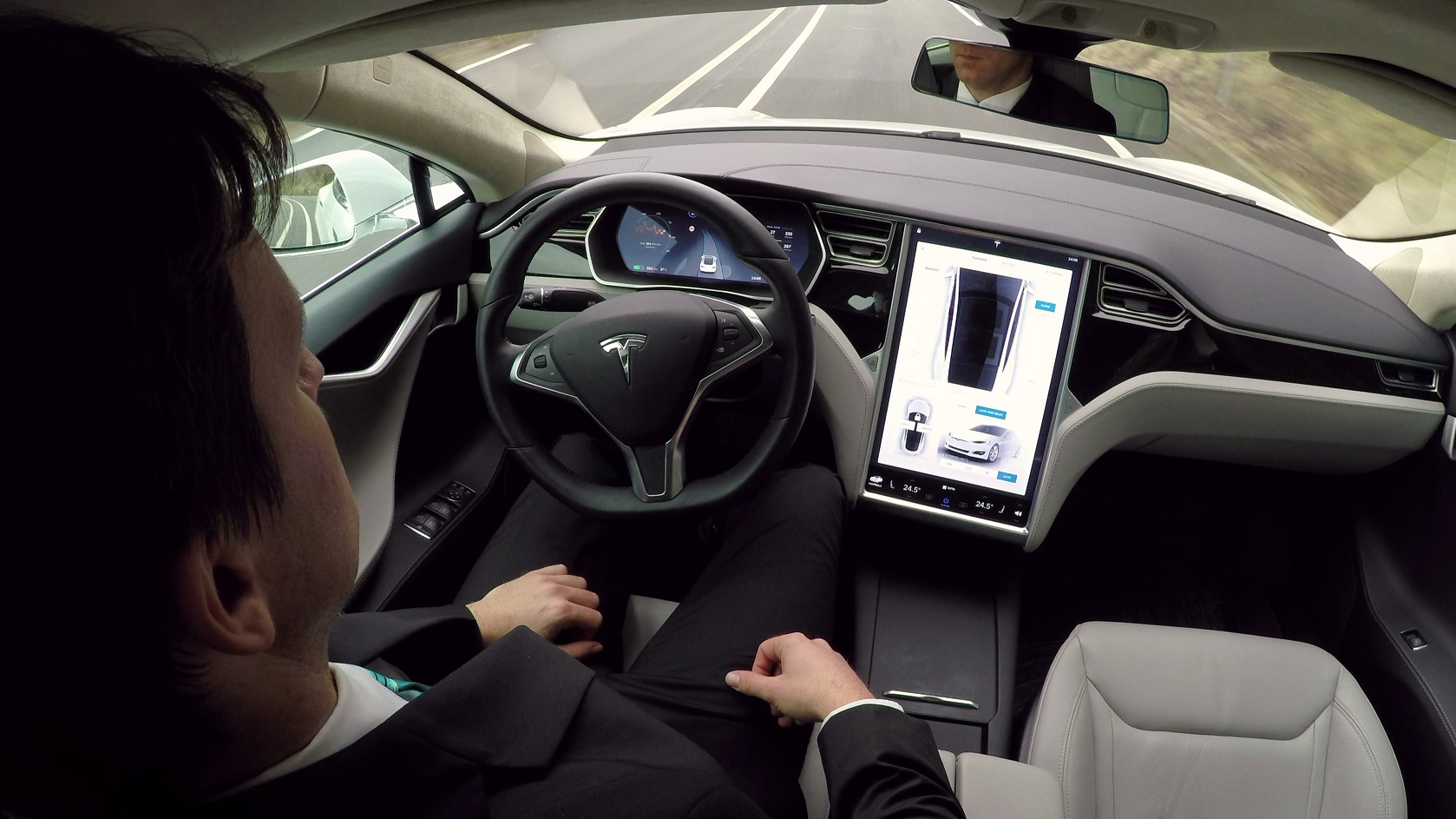 Young businessman traveling to work in luxury Tesla Model S car with enabled autopilot automated self-driving system - 2016