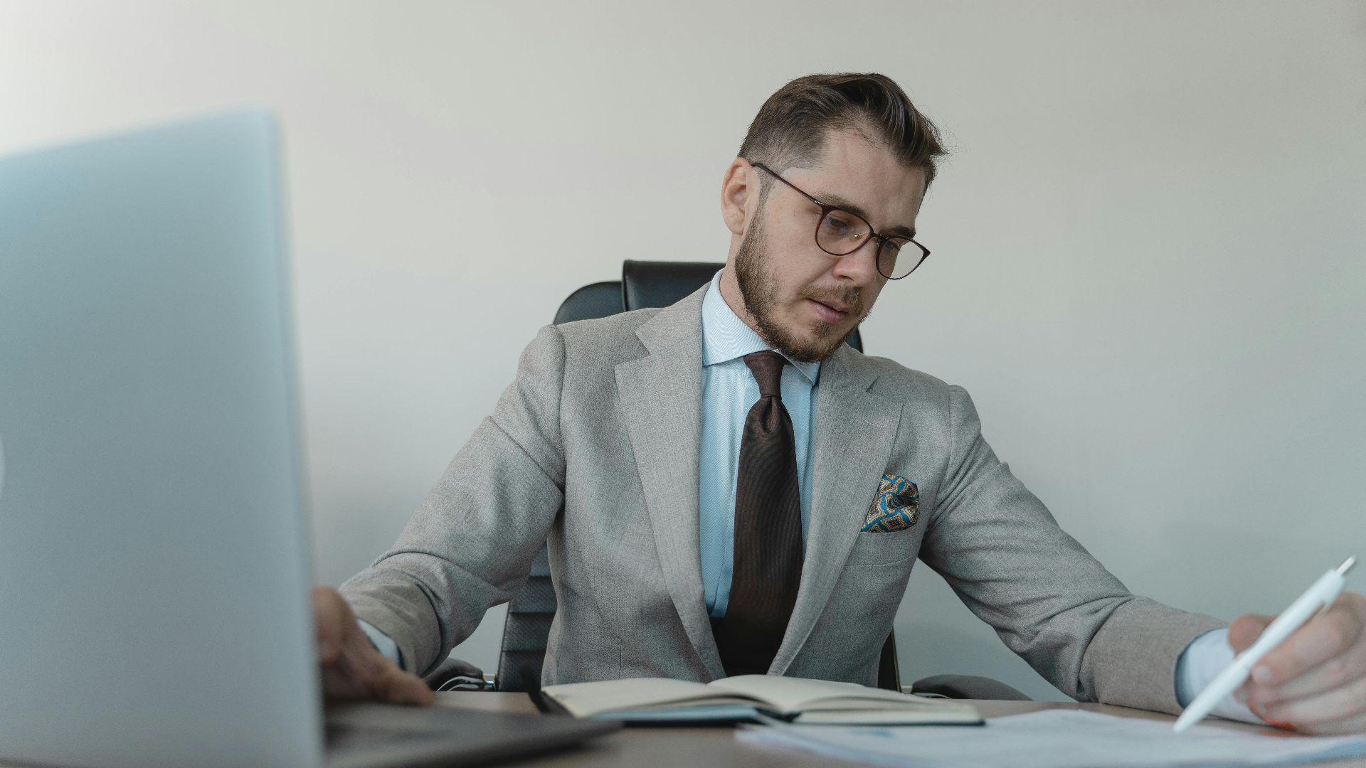 Professional businessman in gray suit working with documents and laptop in modern office.