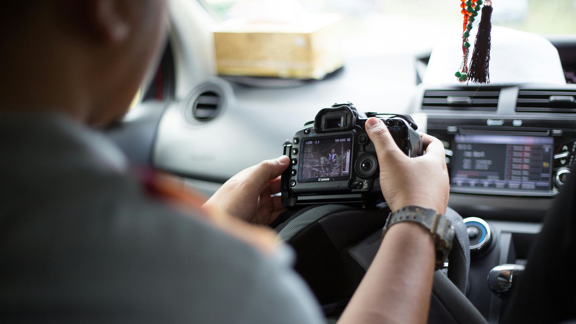 Photographer holding DSLR camera inside car, checking images and settings.