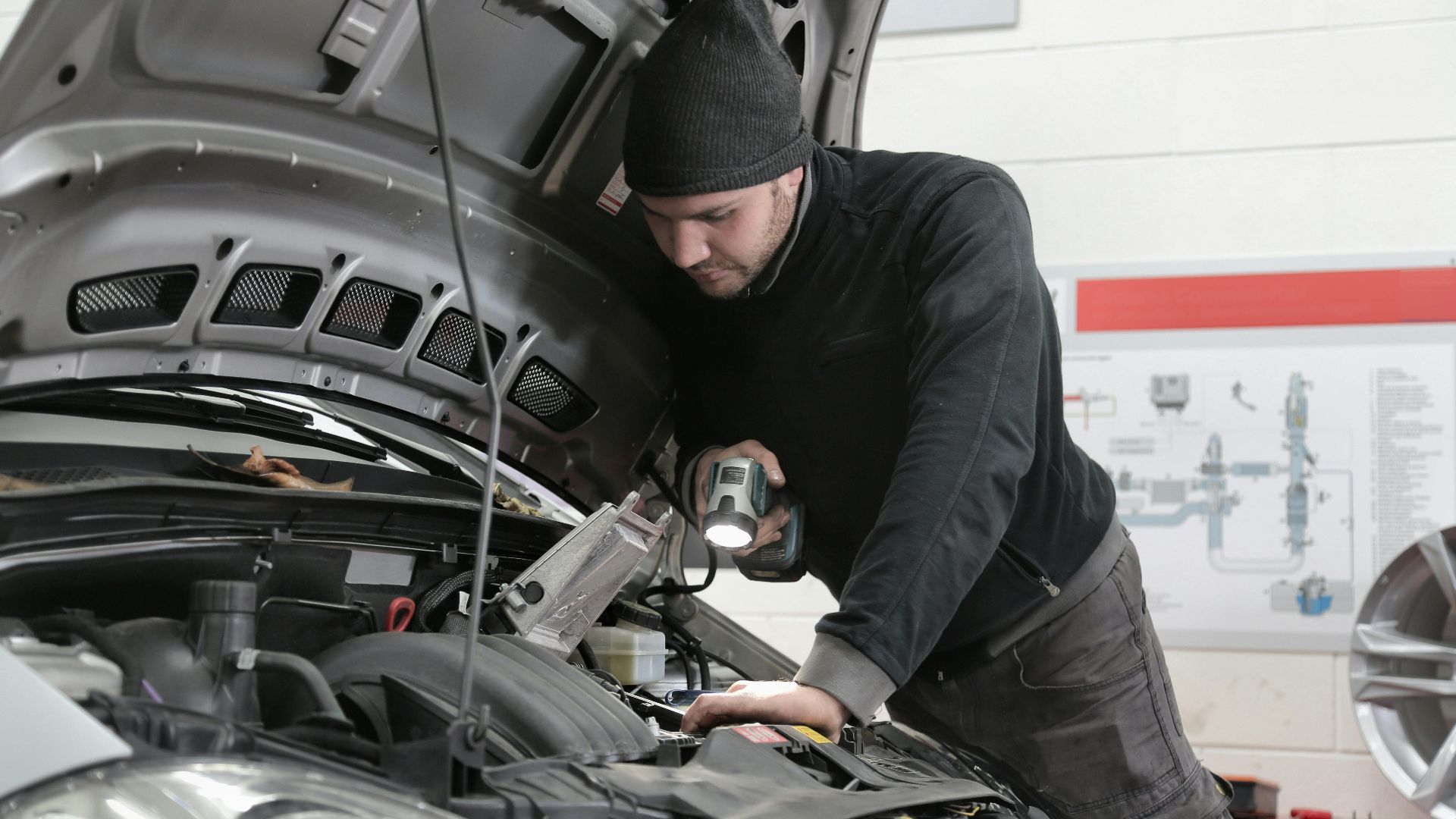 A mechanic closely inspects a car engine in a garage using a flashlight, ensuring proper maintenance.