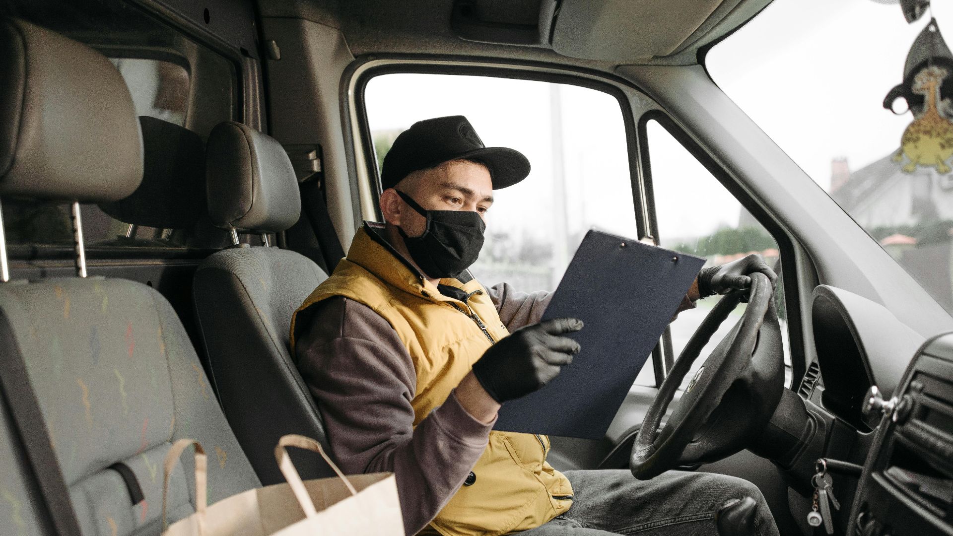 Masked delivery driver reading clipboard in a van during the day.