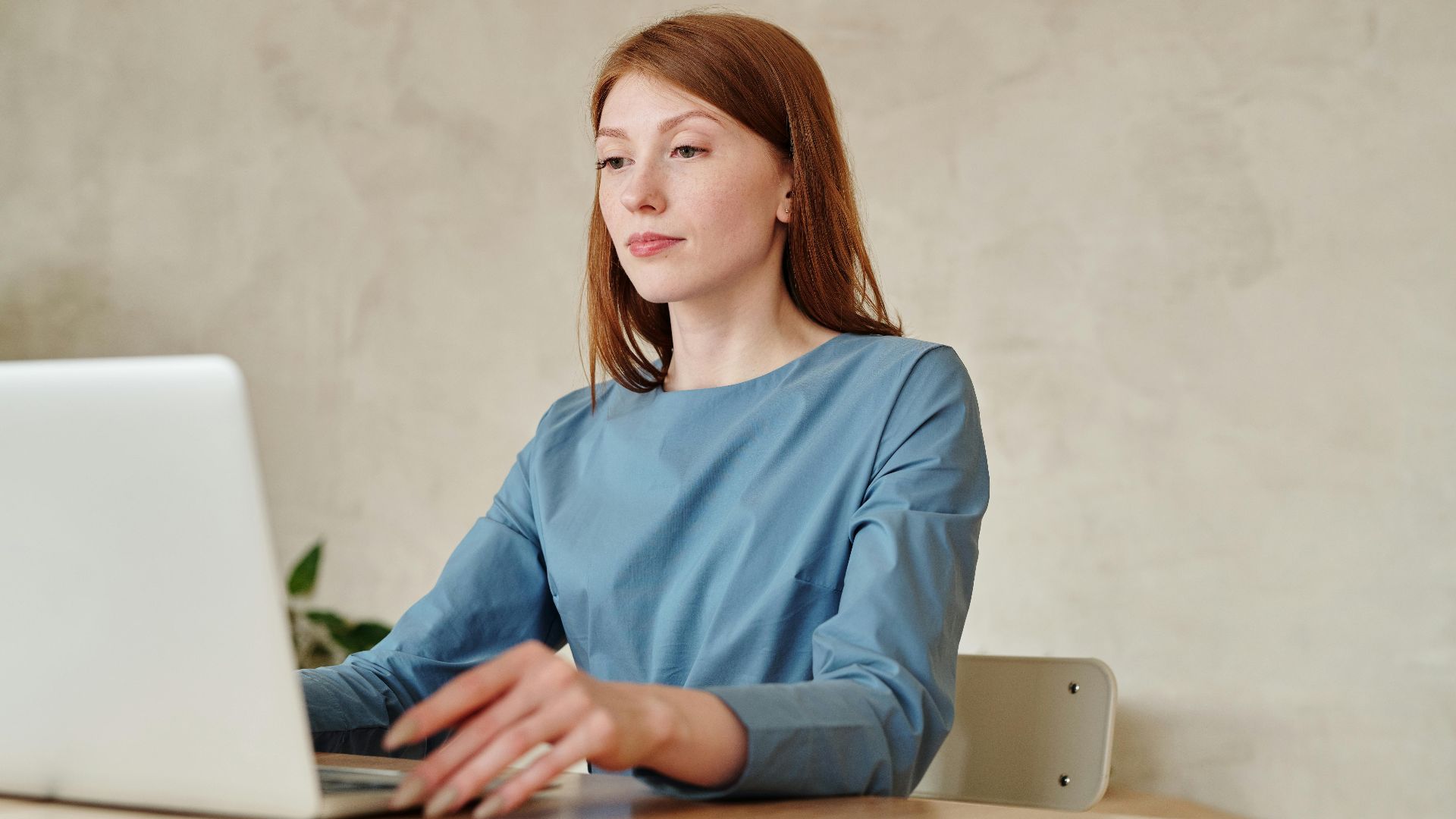 Caucasian woman in blue shirt working on a laptop indoors at home.