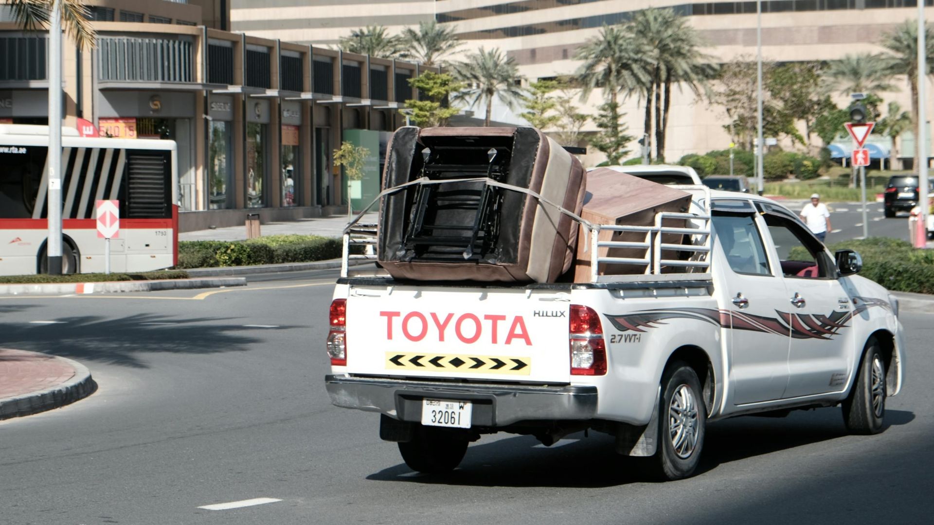 Busy street scene in downtown Dubai with a transport vehicle and bus amidst modern architecture.