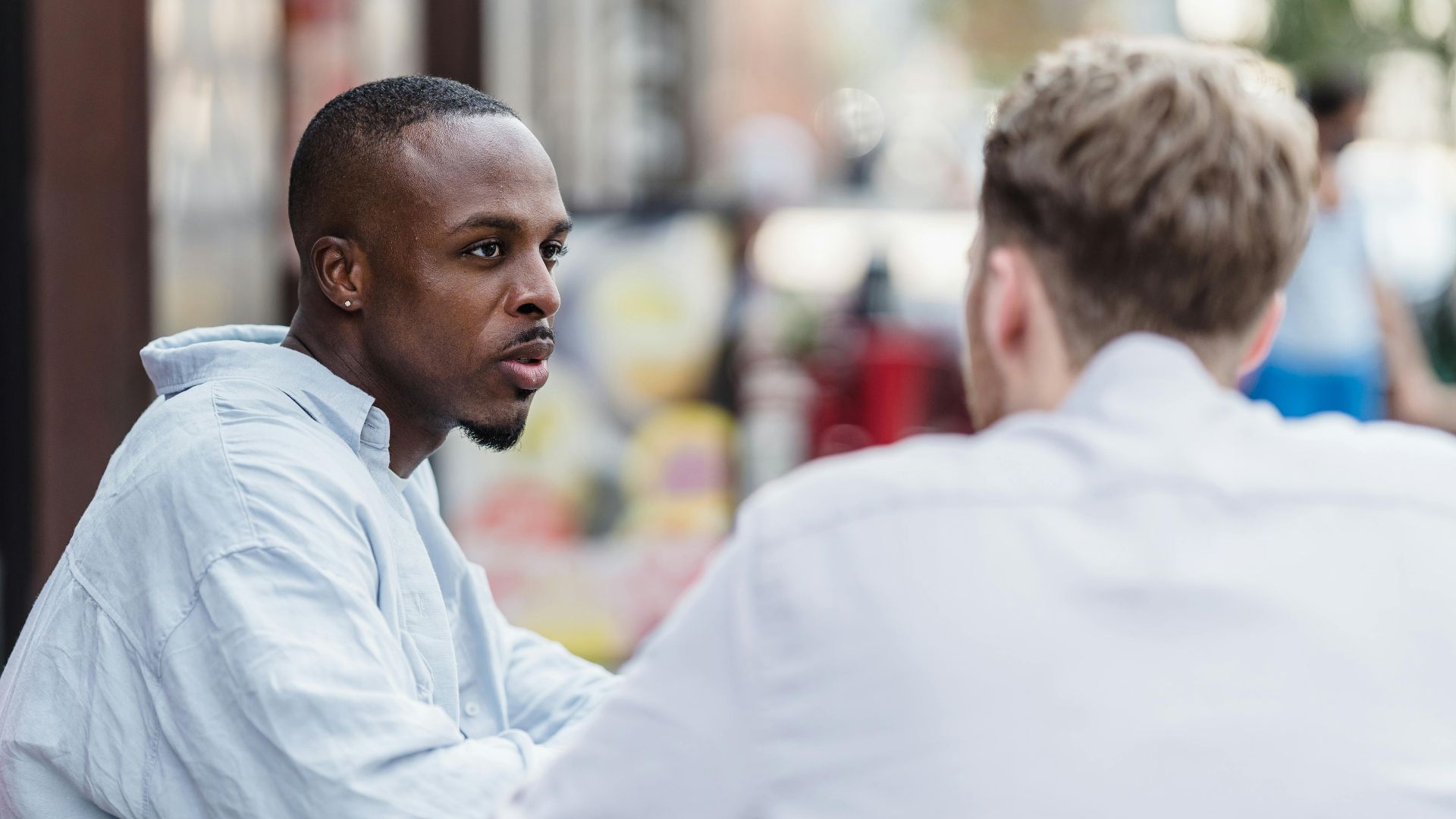 Two men having a conversation in an outdoor setting on a sunny day.