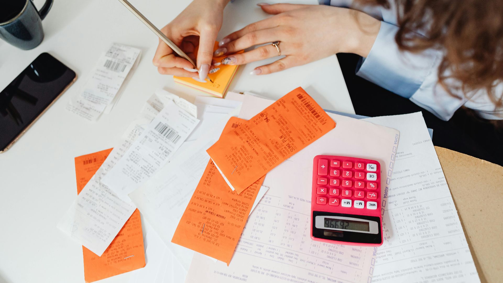 A woman writes down financial details using a calculator, receipts, and documents.