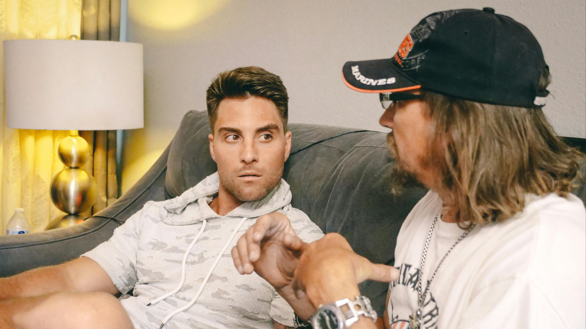Two men having an intense discussion on a couch indoors, focused on one another.