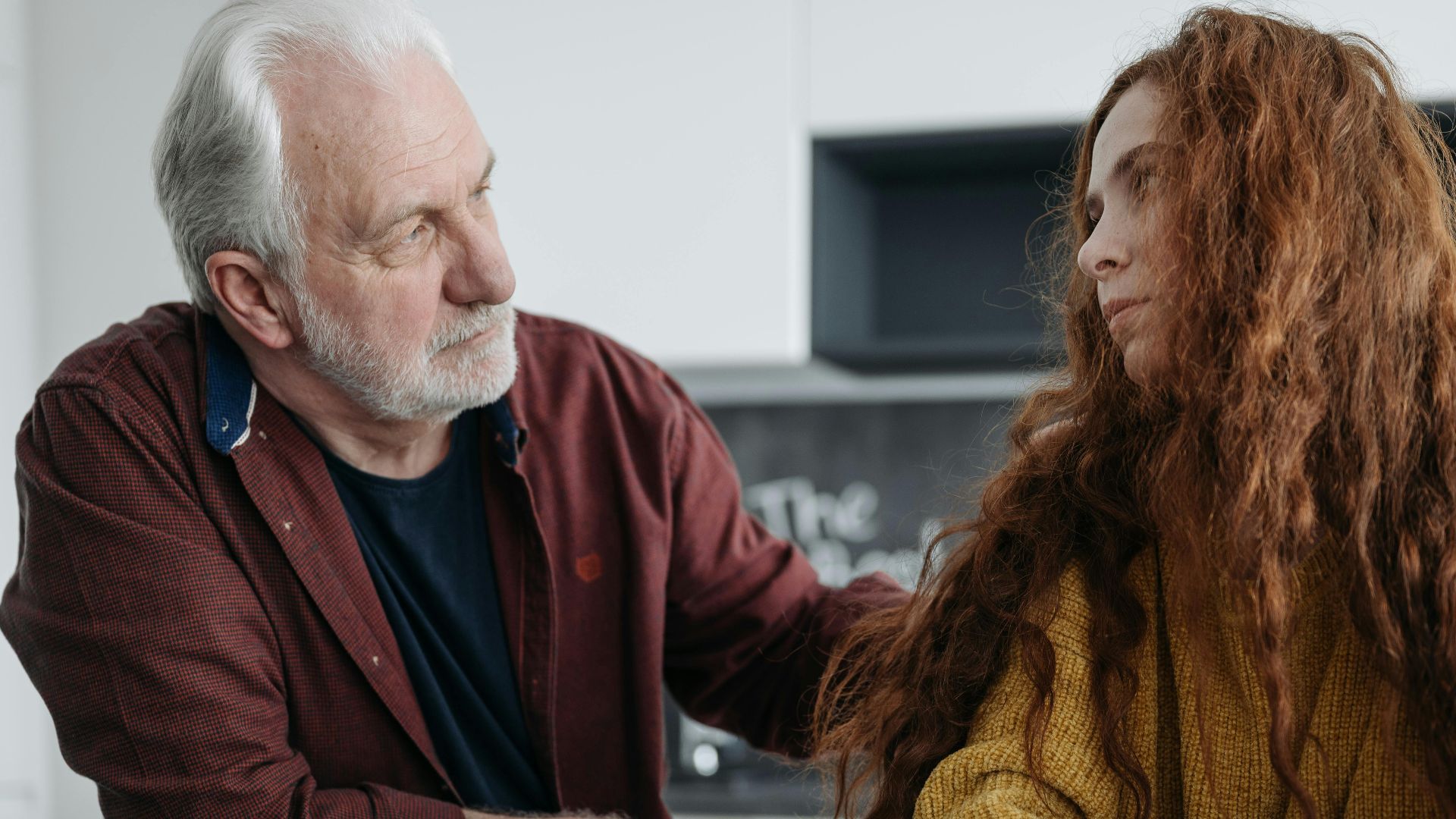 A touching moment between a grandfather and granddaughter sharing emotions indoors over coffee.