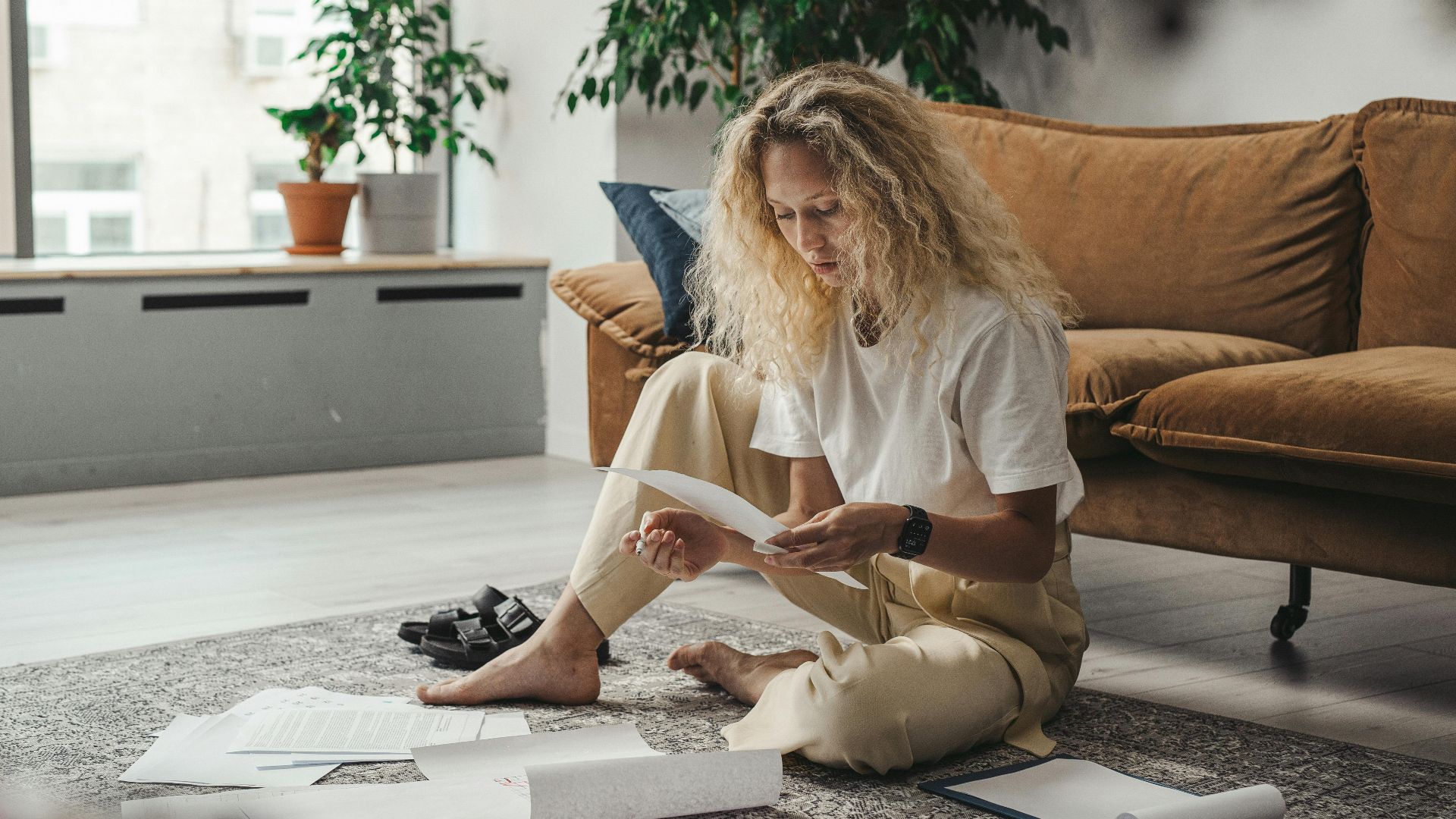 Woman sitting on the floor at home, reviewing paperwork in a relaxed environment.