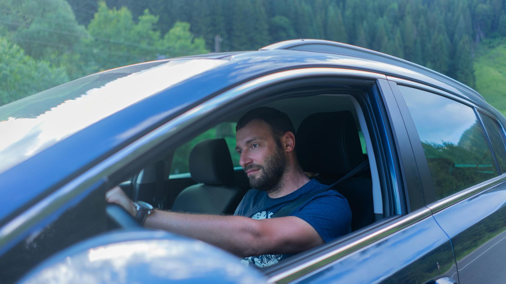 Bearded man enjoying a drive through lush green countryside on a sunny day.