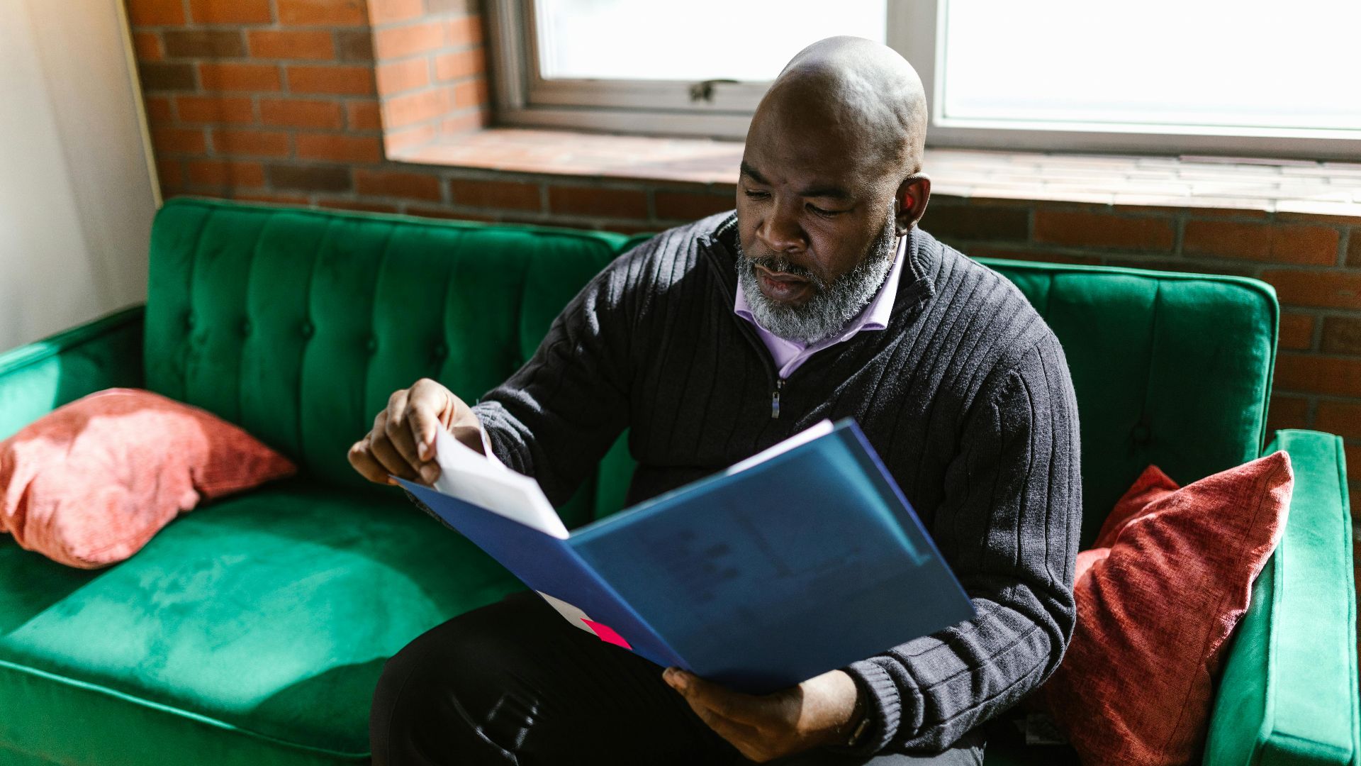 African American adult man reviewing documents on a green sofa, indoors.