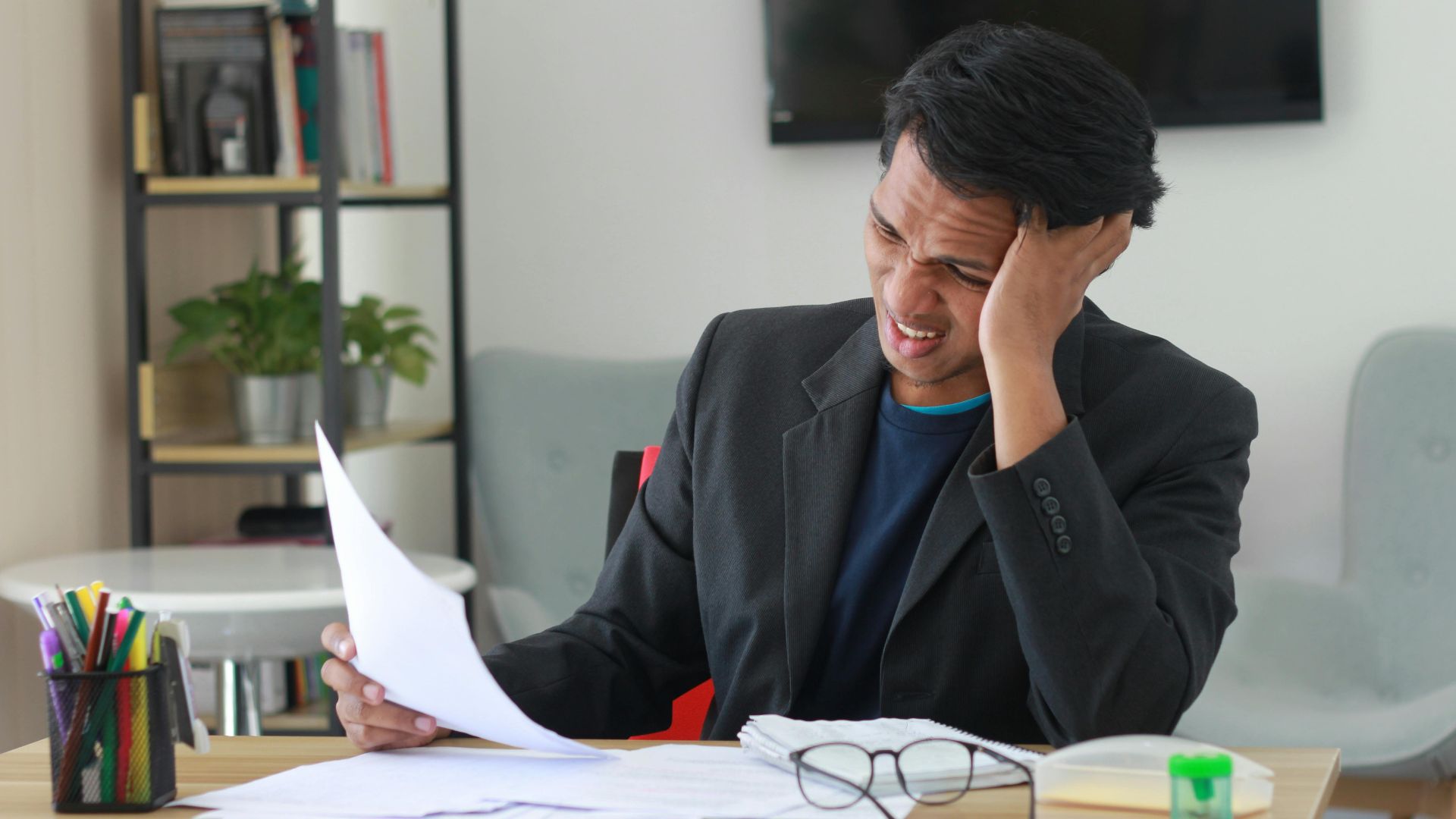 A businessman in an office experiencing stress while reviewing documents.