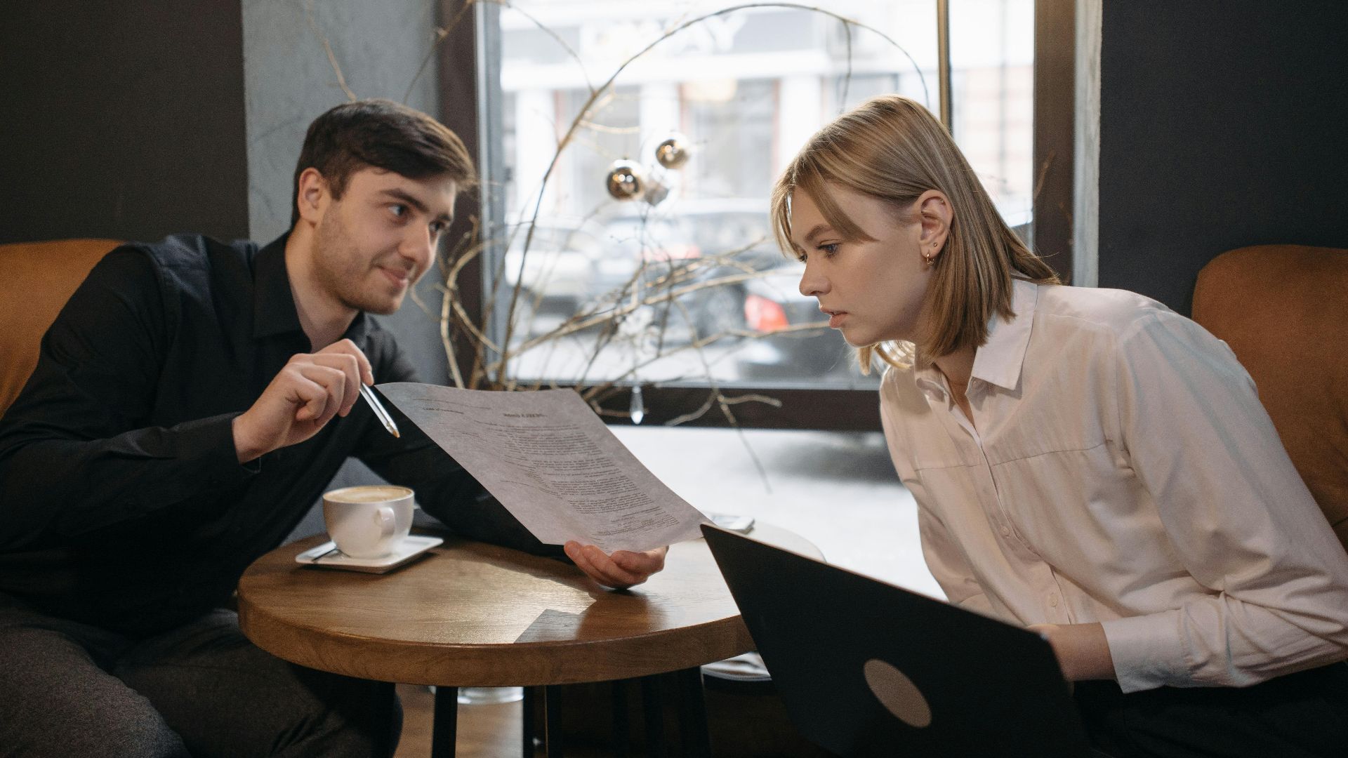 Engaged colleagues discussing documents over coffee in a cozy cafe setting.