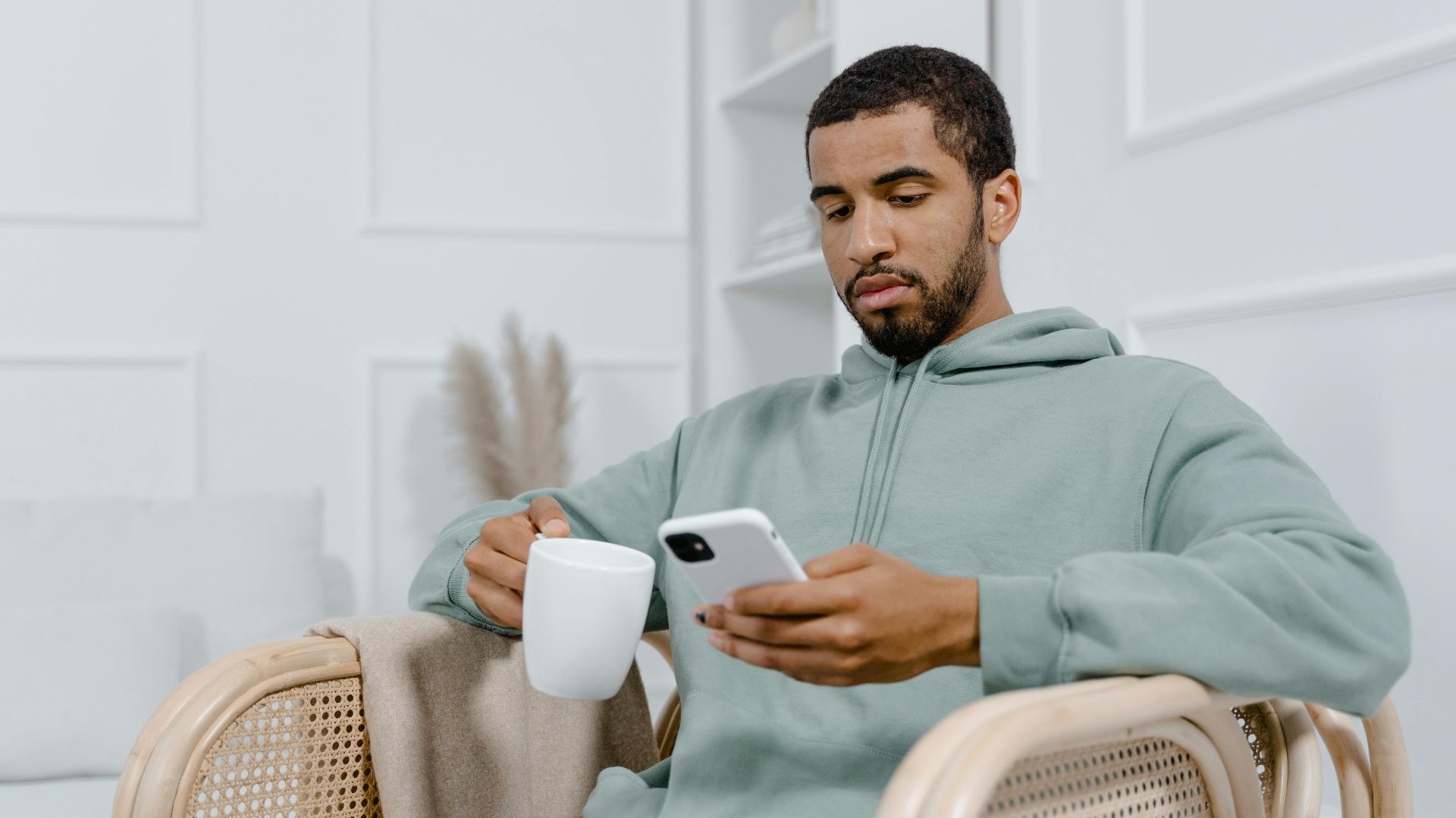 Young man in a grey hoodie sits with a coffee mug and smartphone, exuding a relaxed vibe.