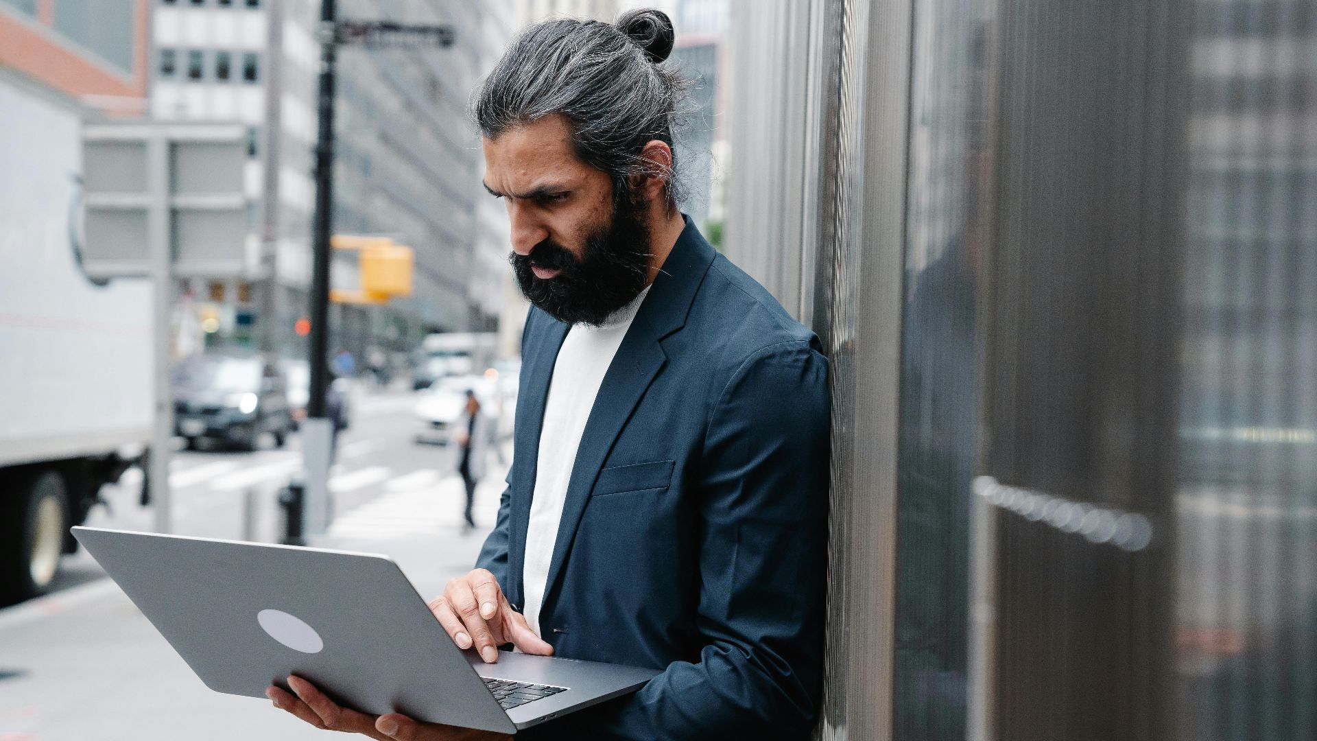 Bearded businessman focusing on laptop work in an urban outdoor setting.
