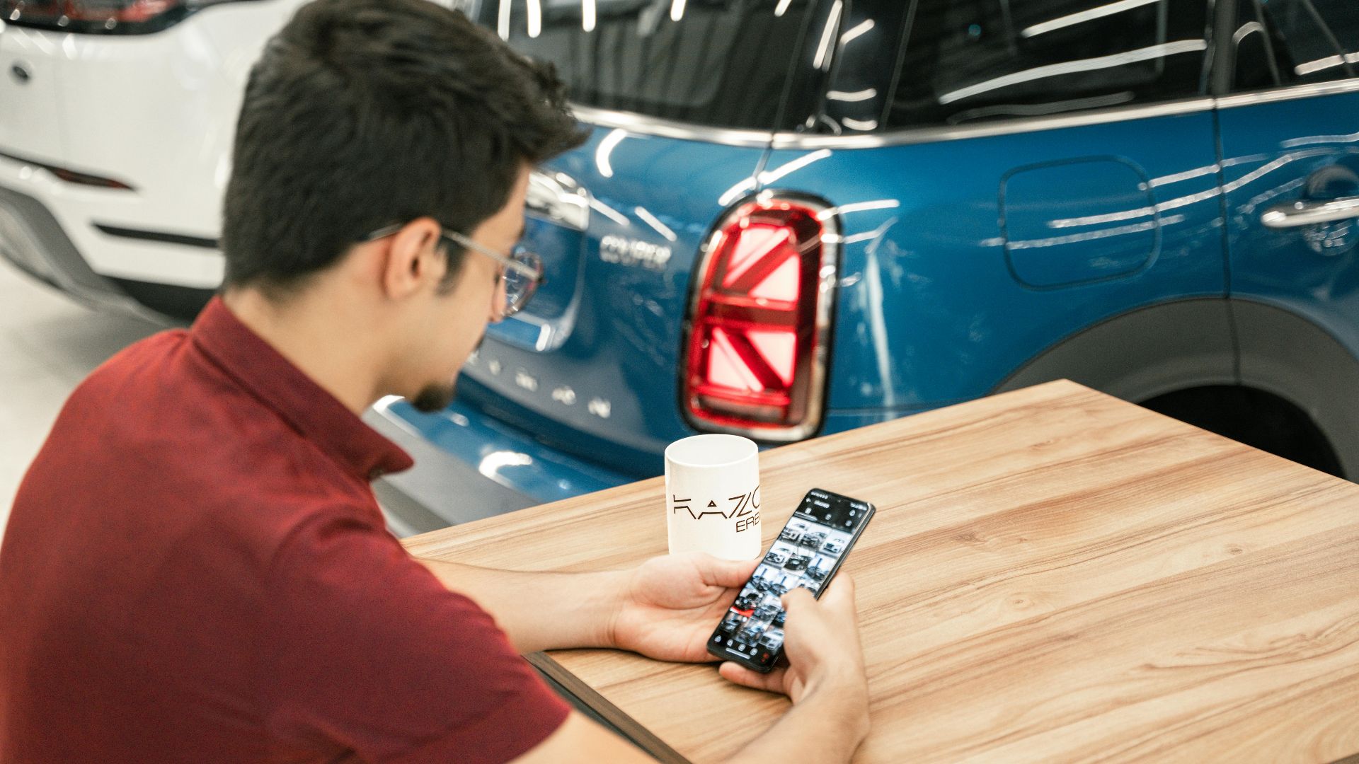 Young man at car dealership using smartphone. Modern cars in background.