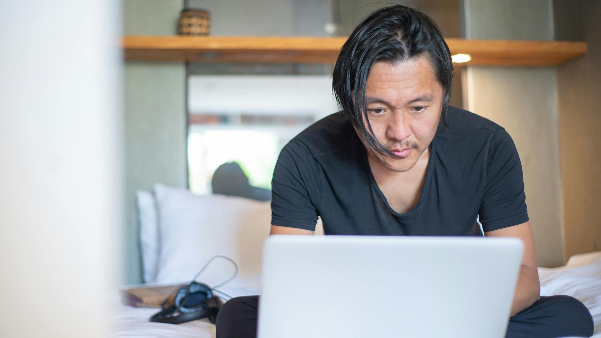 An Asian man working from home on a laptop, focusing on his digital tasks in a cozy indoor setting.