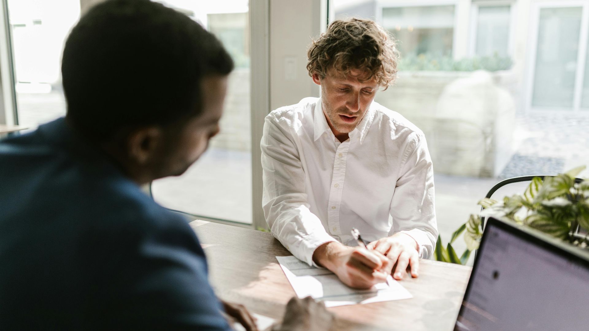 Two men collaborating in a modern office, reviewing and signing documents.