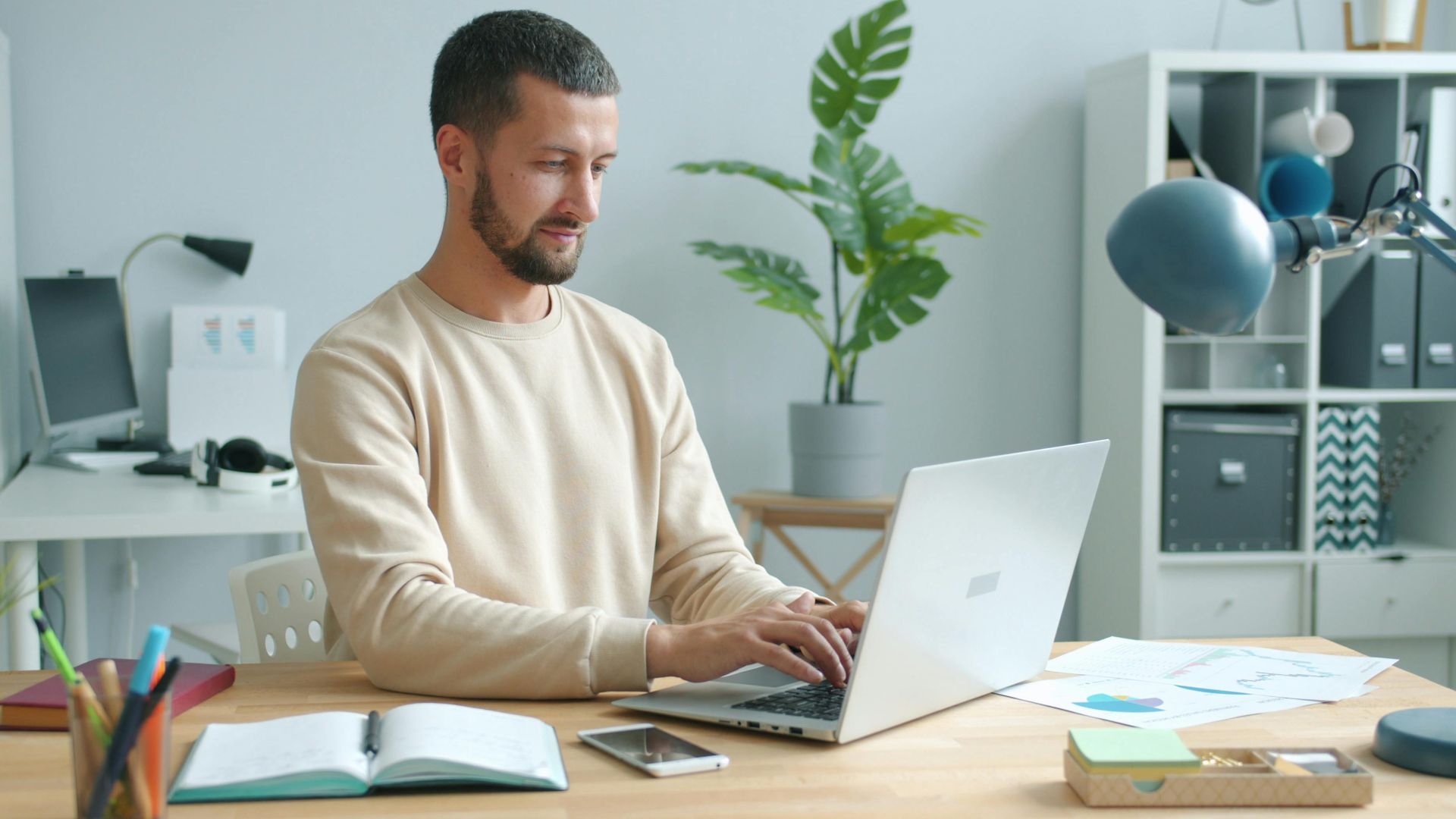 Man typing on a laptop in a modern home office setup with plants.