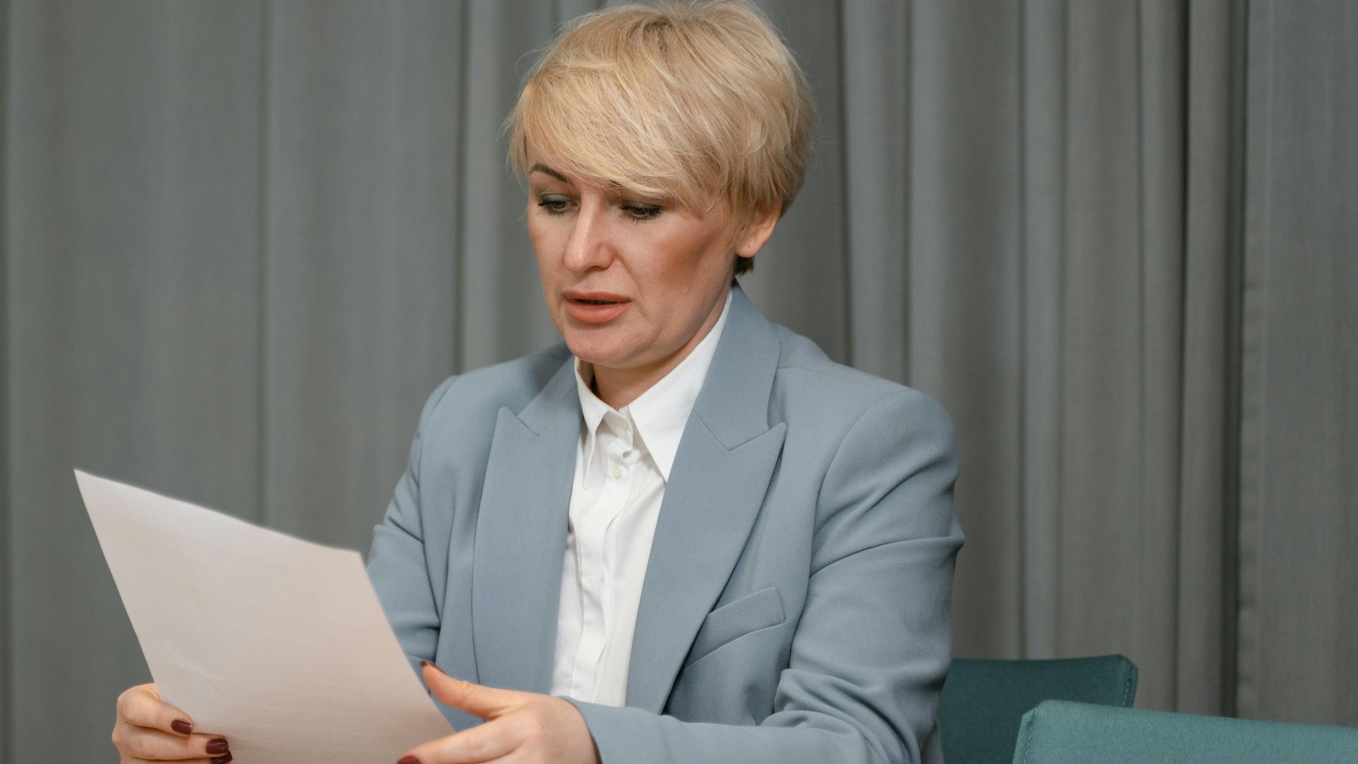 Businesswoman in a blazer reviewing documents at a desk. Professional office setting with laptop and papers.