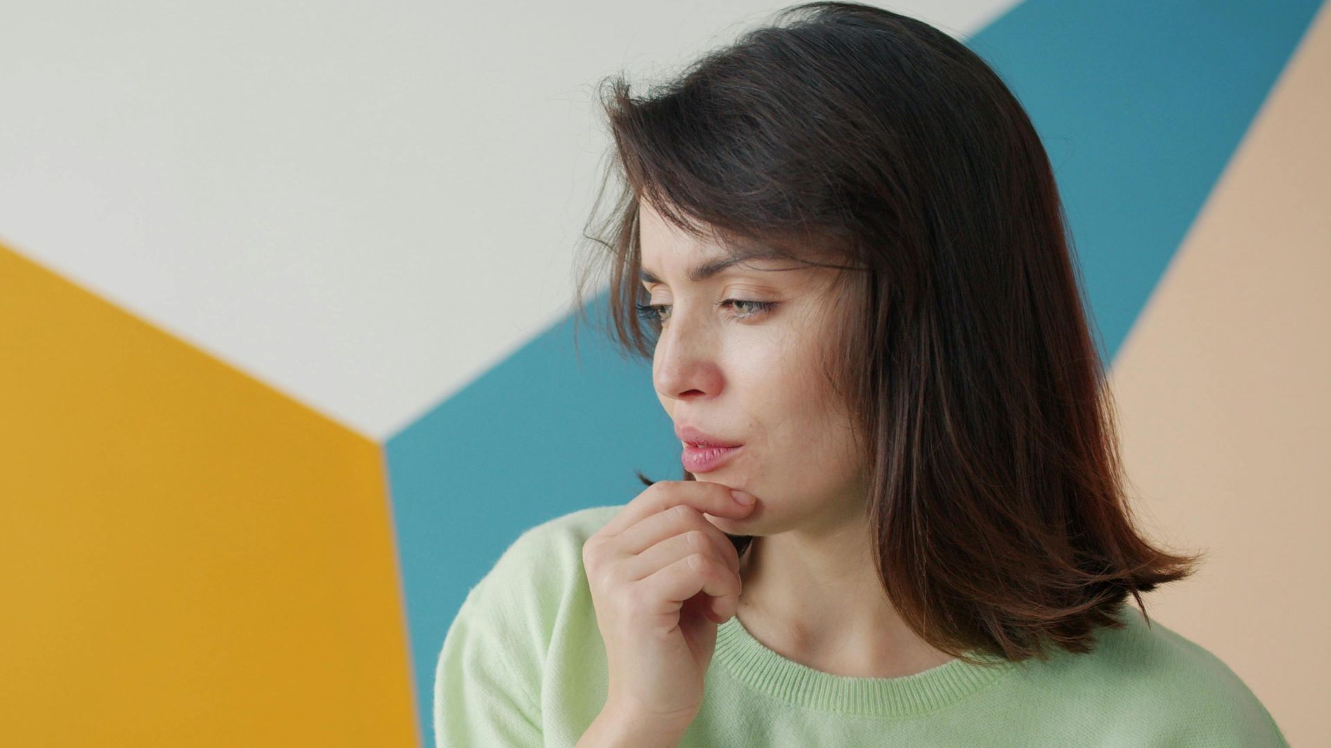 Young woman in contemplation against a colorful geometric background, indoors.