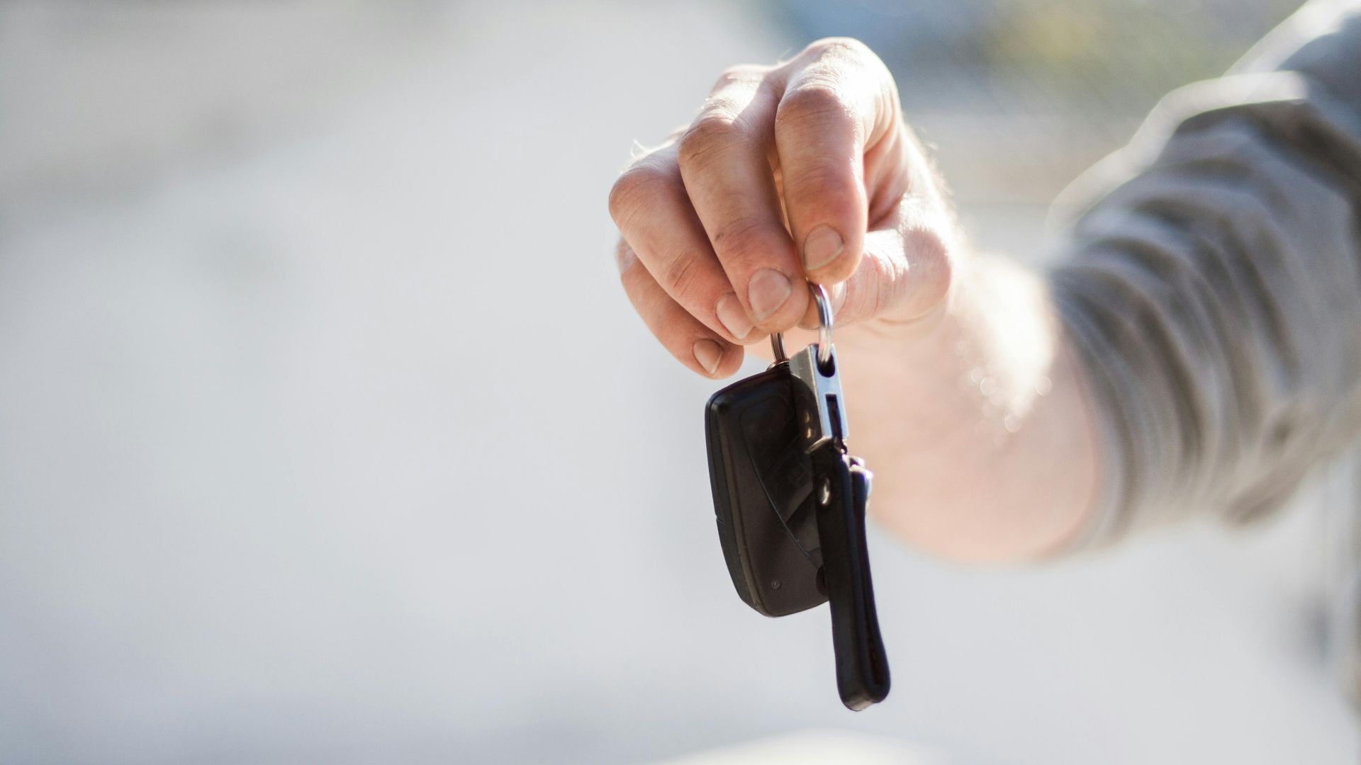 Close-up of a hand handing over car keys, signifying purchase or rental.