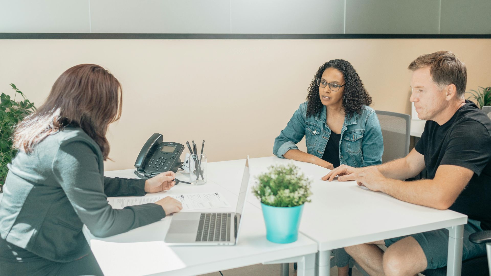 Anonymous female employee interacting with diverse clients at table with netbook and paper sheet in workspace