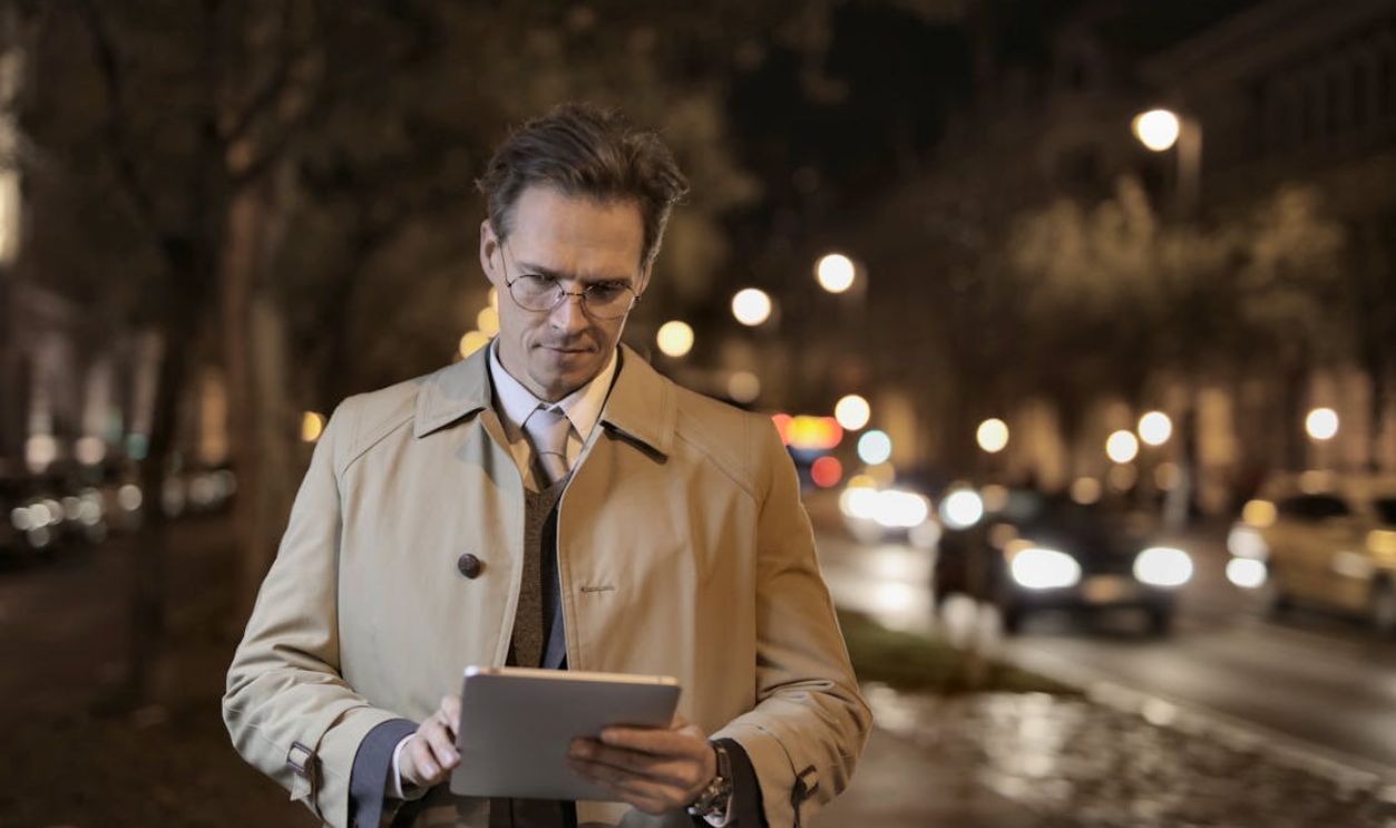 Confident man using a tablet on a city street at night, blending technology and business