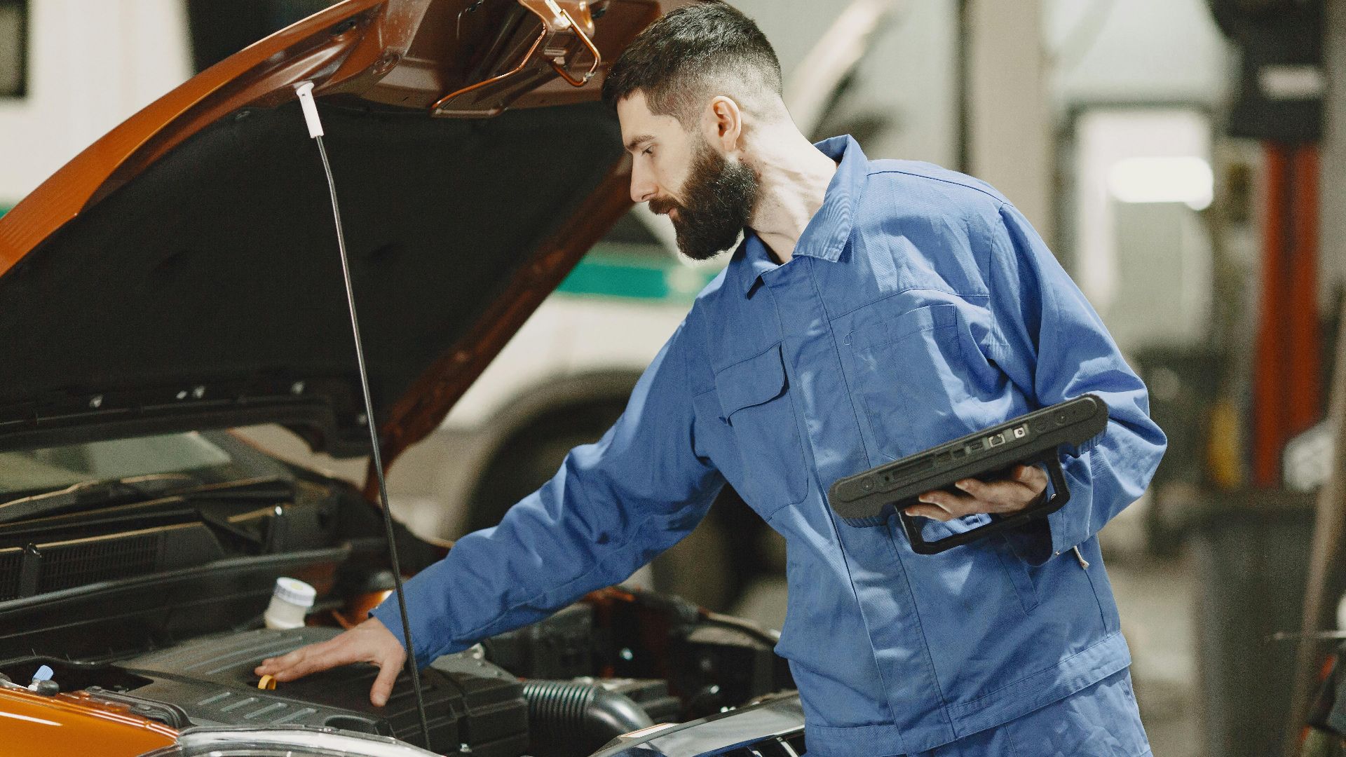 Professional mechanic examining a car engine under an open hood in a garage setting.