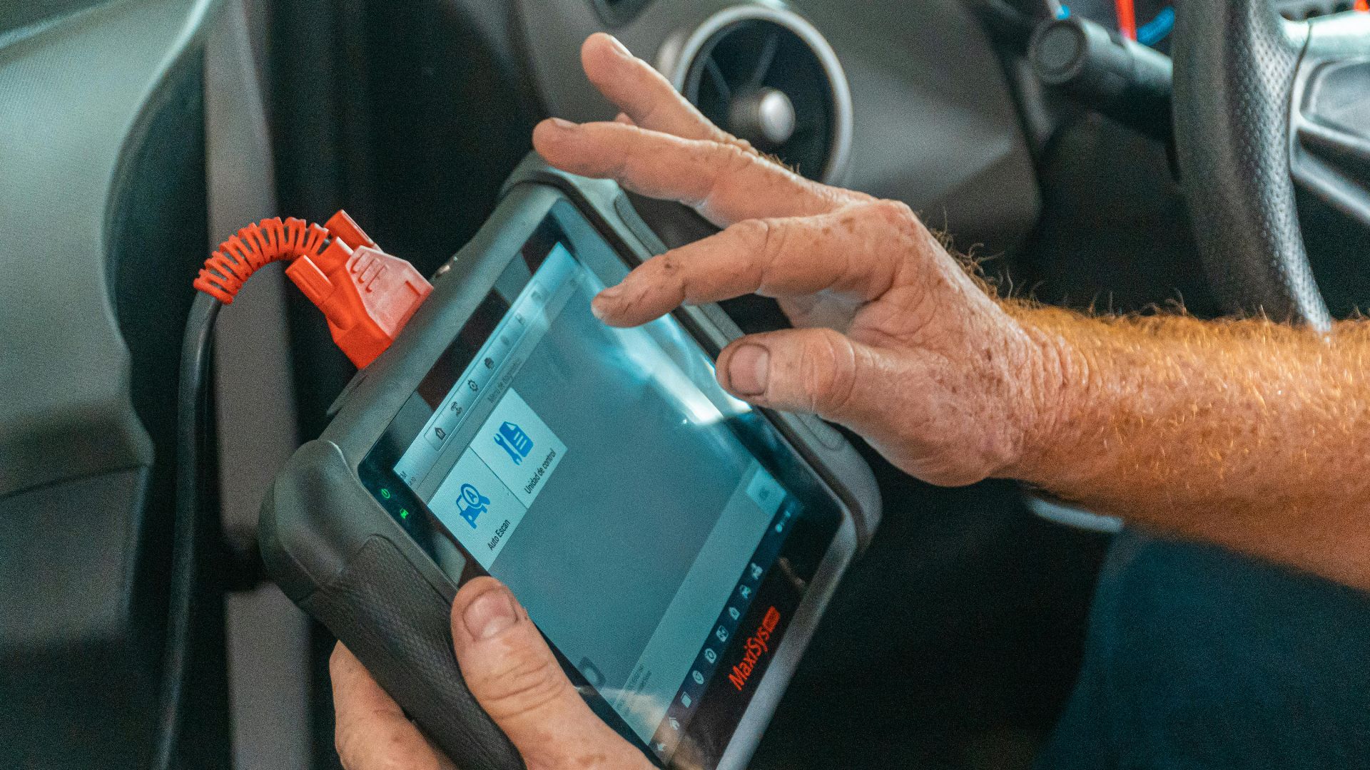 Mechanic using a diagnostic tool inside a car to check for engine issues and ensure proper maintenance.