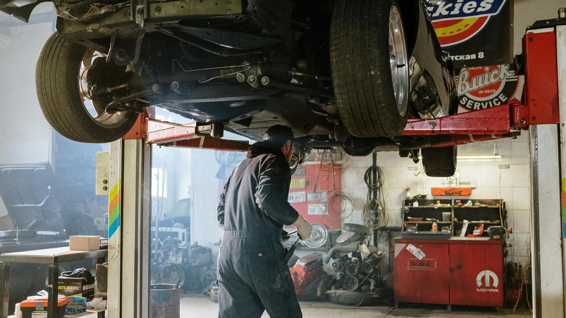 Mechanic repairing a vehicle in a busy workshop with various automotive tools.