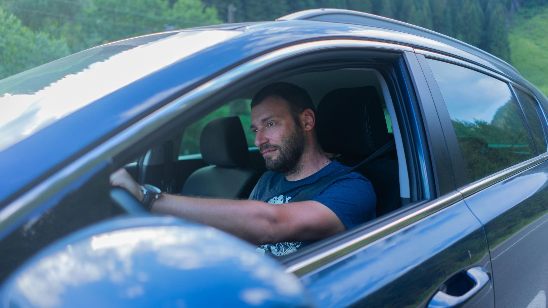 Bearded man enjoying a drive through lush green countryside on a sunny day.