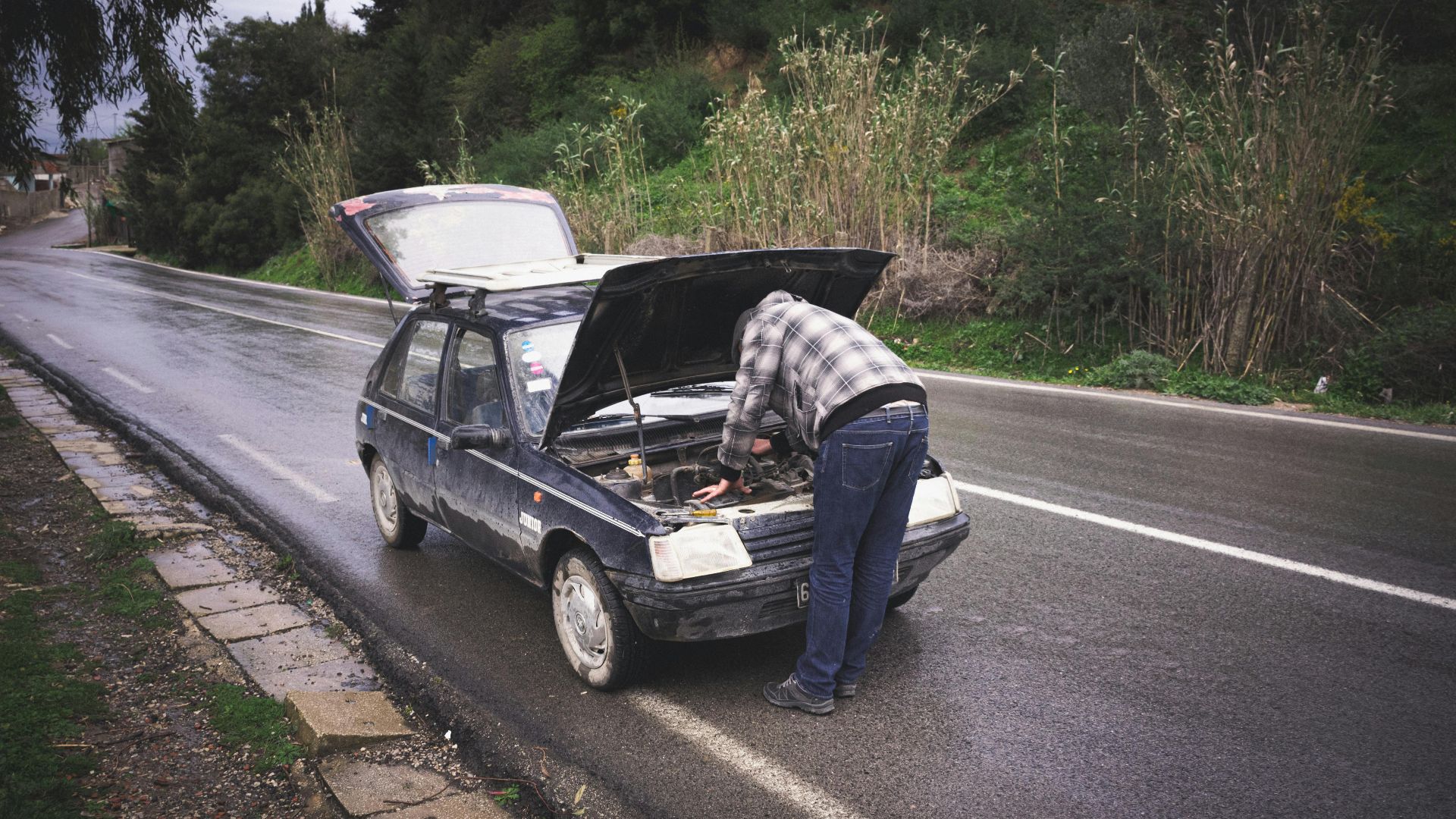 An individual repairing a car on a rainy road in Tabarka, showcasing urgent roadside vehicle maintenance.