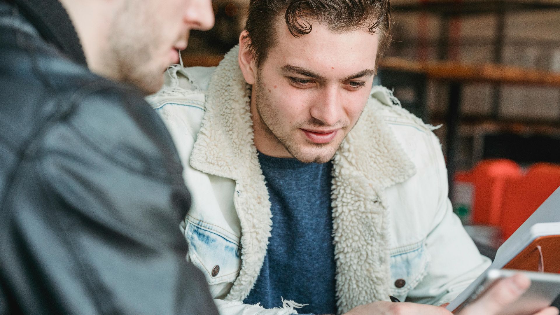 Male worker looking at screen of tablet while discussing strategy of project with crop partner in cafe